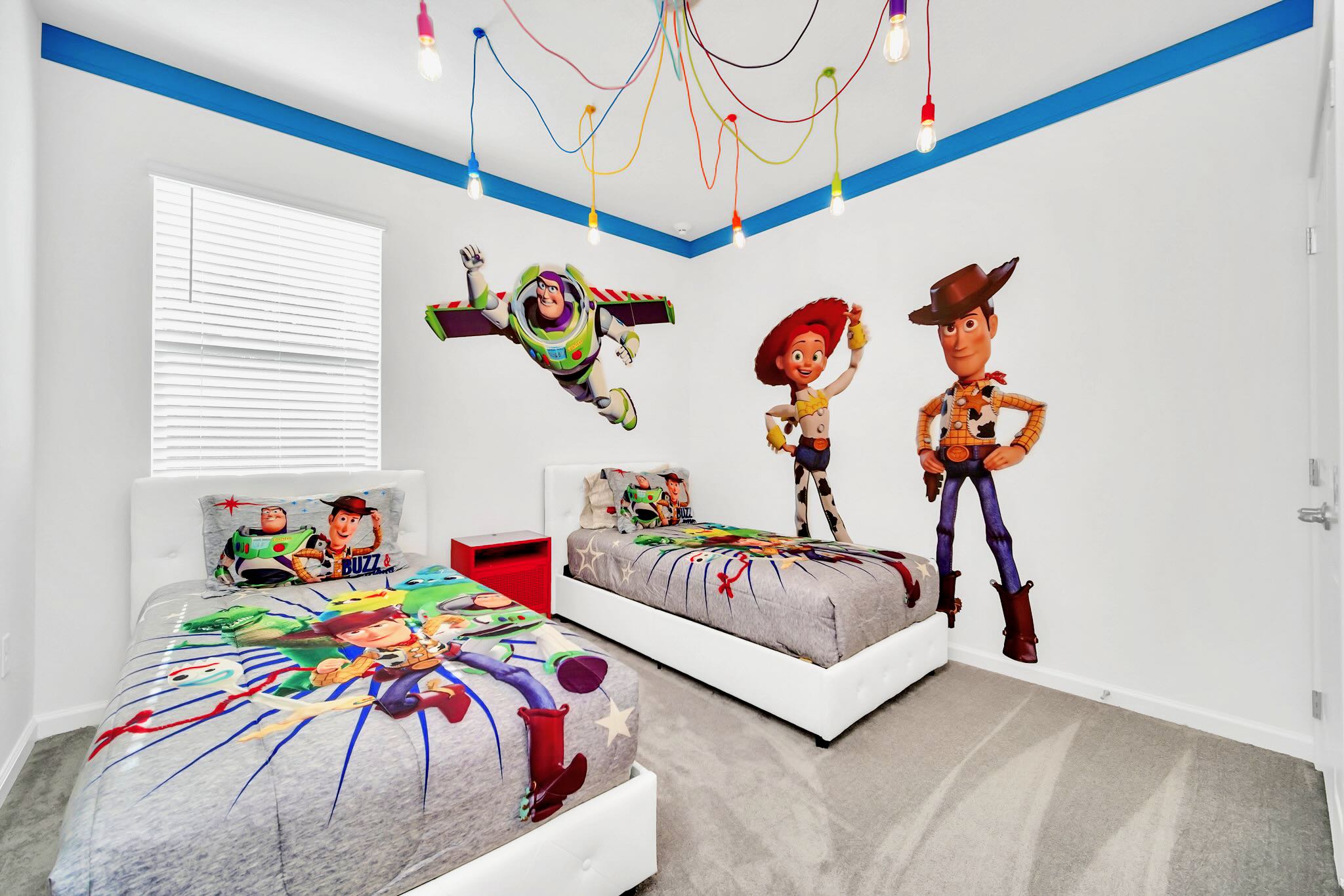 A fun Toy Story themed bedroom with two twin beds, colorful character bedding, large wall decals of Buzz Lightyear, Jessie, and Woody, and a unique multi-colored exposed bulb ceiling light fixture.