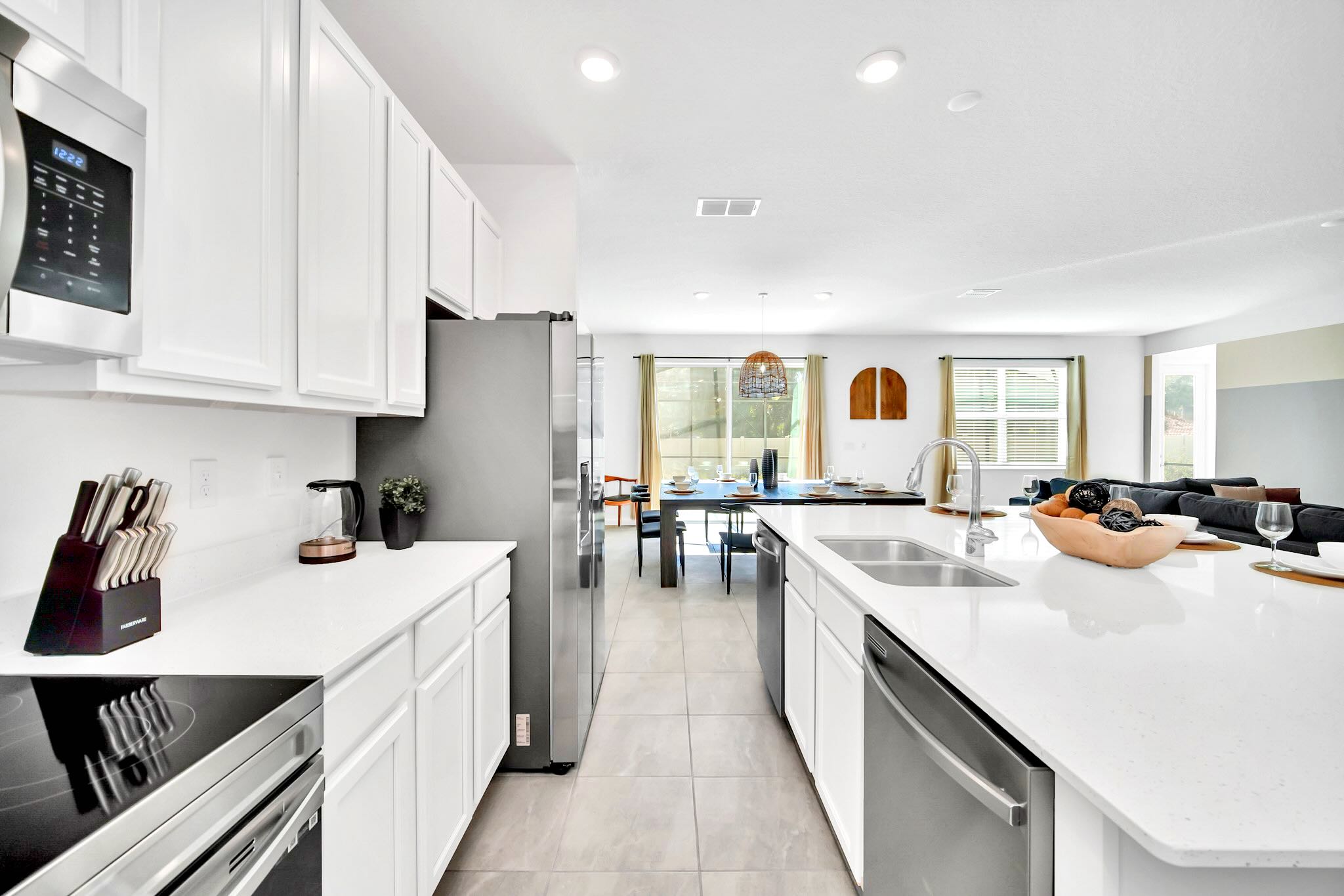 Sleek modern kitchen with white shaker-style cabinets, white quartz countertops, stainless steel appliances including a refrigerator and microwave, and a large island with a sink.