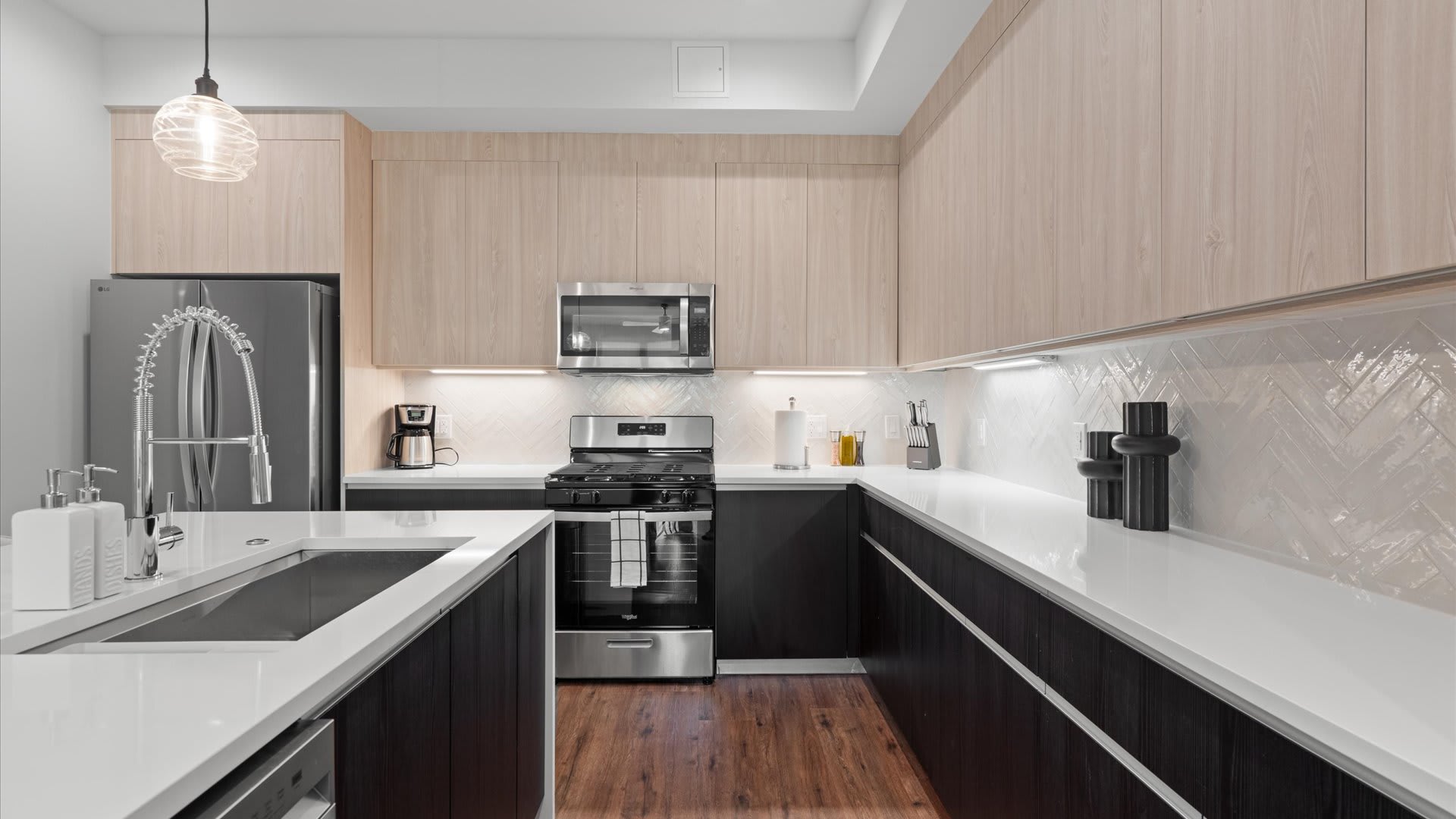 Well-appointed kitchen featuring dark lower cabinets and light wood upper cabinets, white quartz countertops, and a white herringbone tile backsplash. Stainless steel appliances include a gas range, microwave, and a large French door refrigerator.