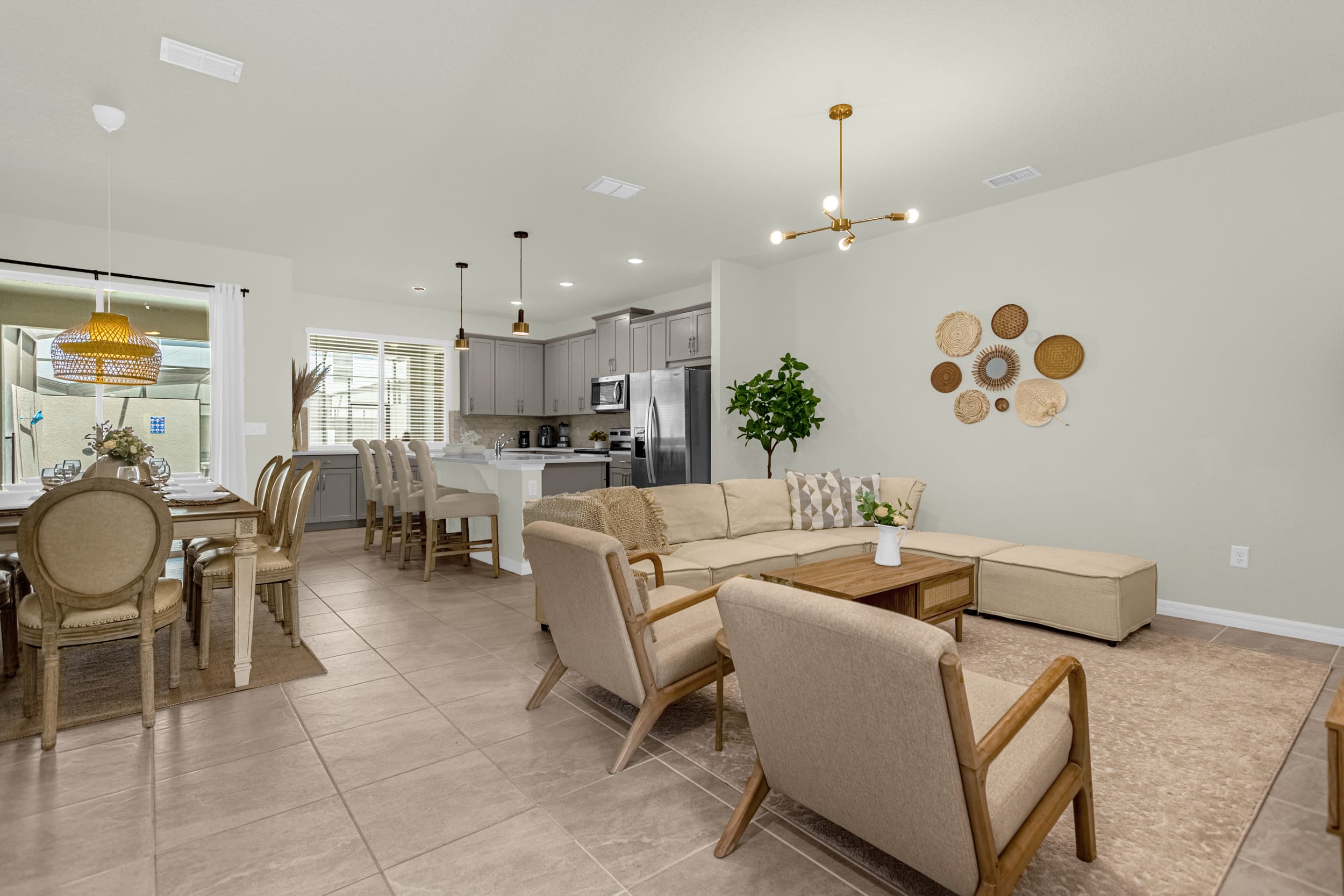Expansive open-concept living area with a large L-shaped sectional sofa, two armchairs, and a wooden coffee table, flowing into the dining and kitchen areas. The space is decorated with neutral tones and natural textures.
