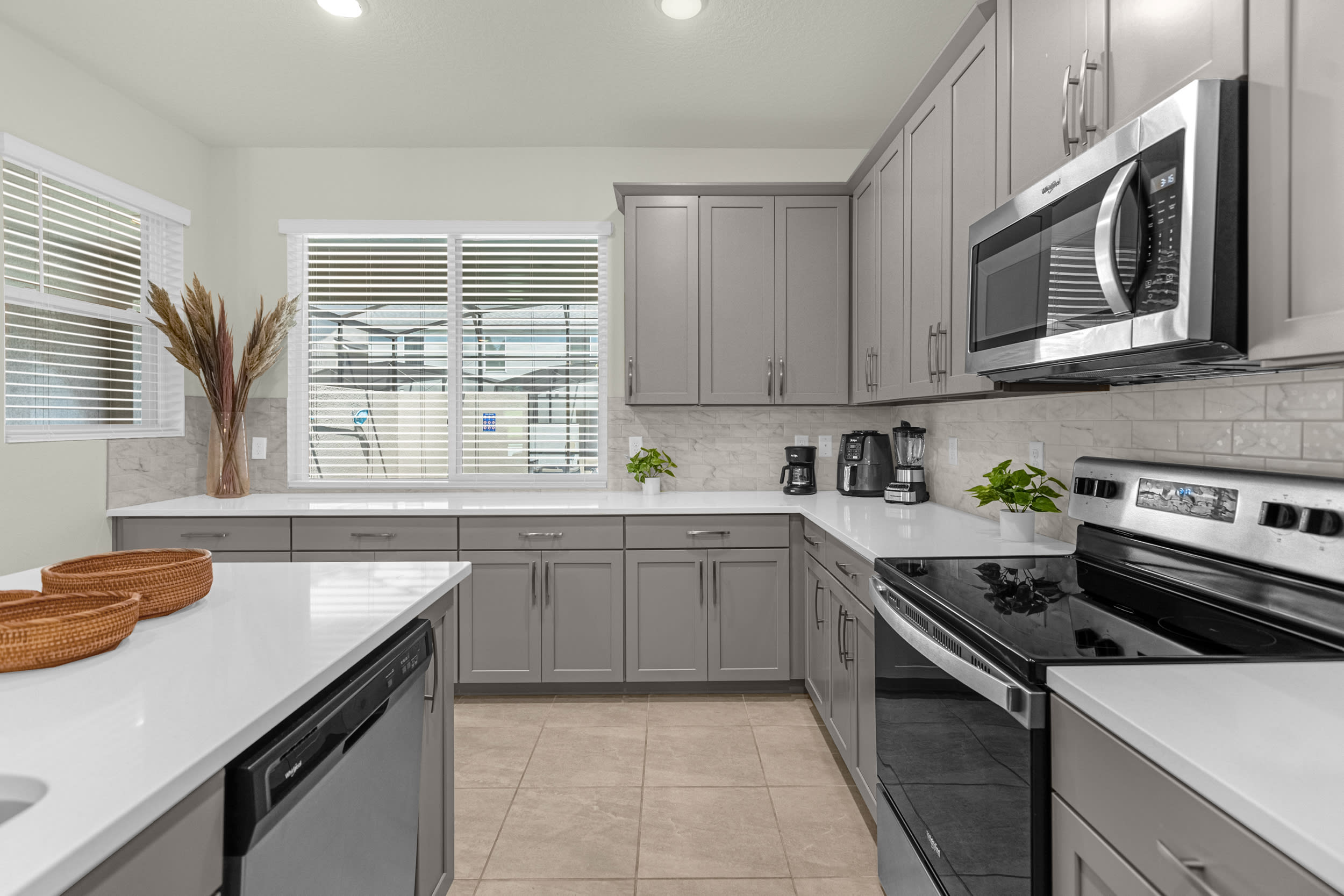 Modern kitchen featuring light gray shaker cabinets, white quartz countertops, a white subway tile backsplash, and stainless steel appliances including a microwave and electric range.