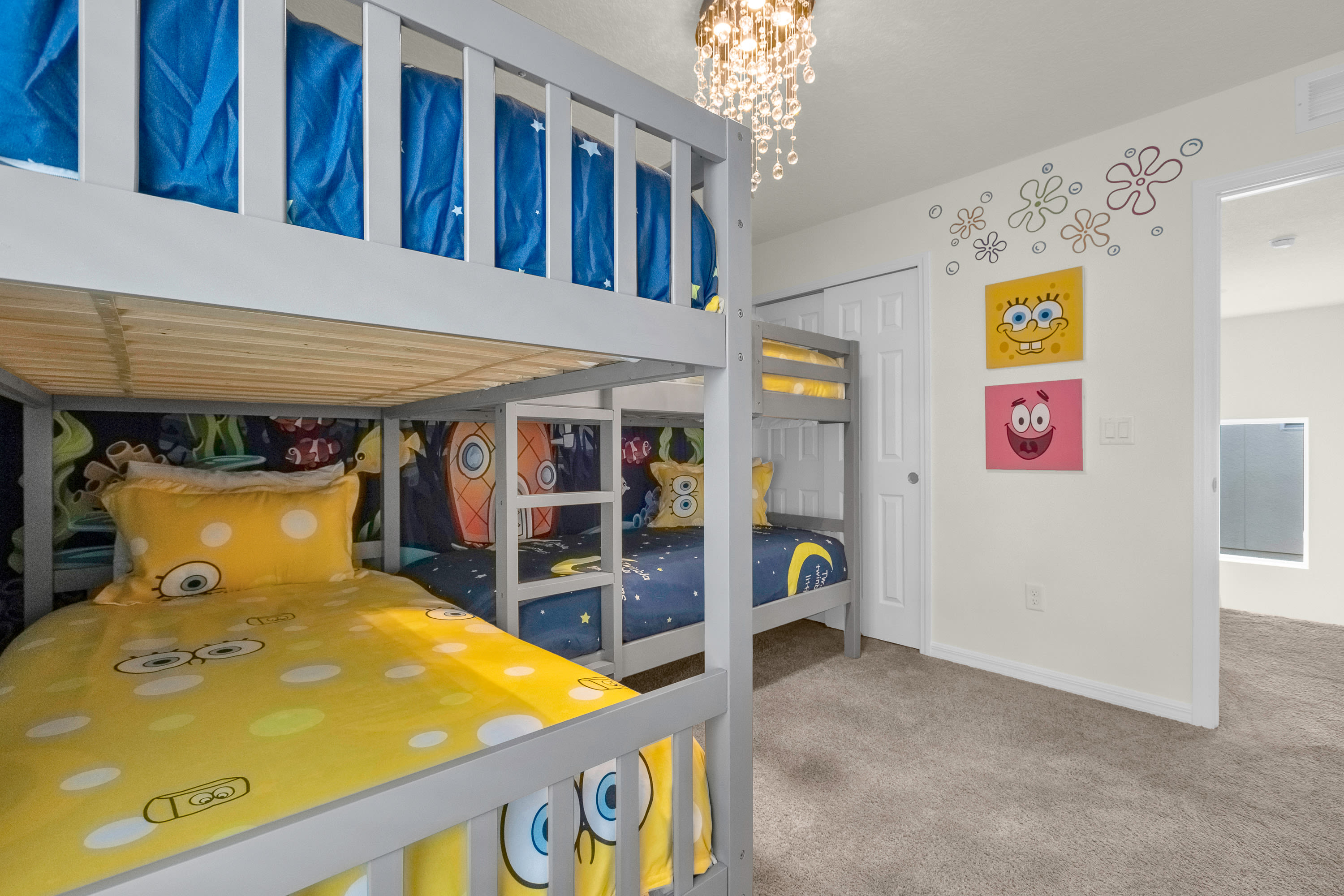 A playful Spongebob-themed bedroom showcasing two gray bunk beds with colorful bedding, a closet with white bi-fold doors, and Spongebob artwork on the wall.