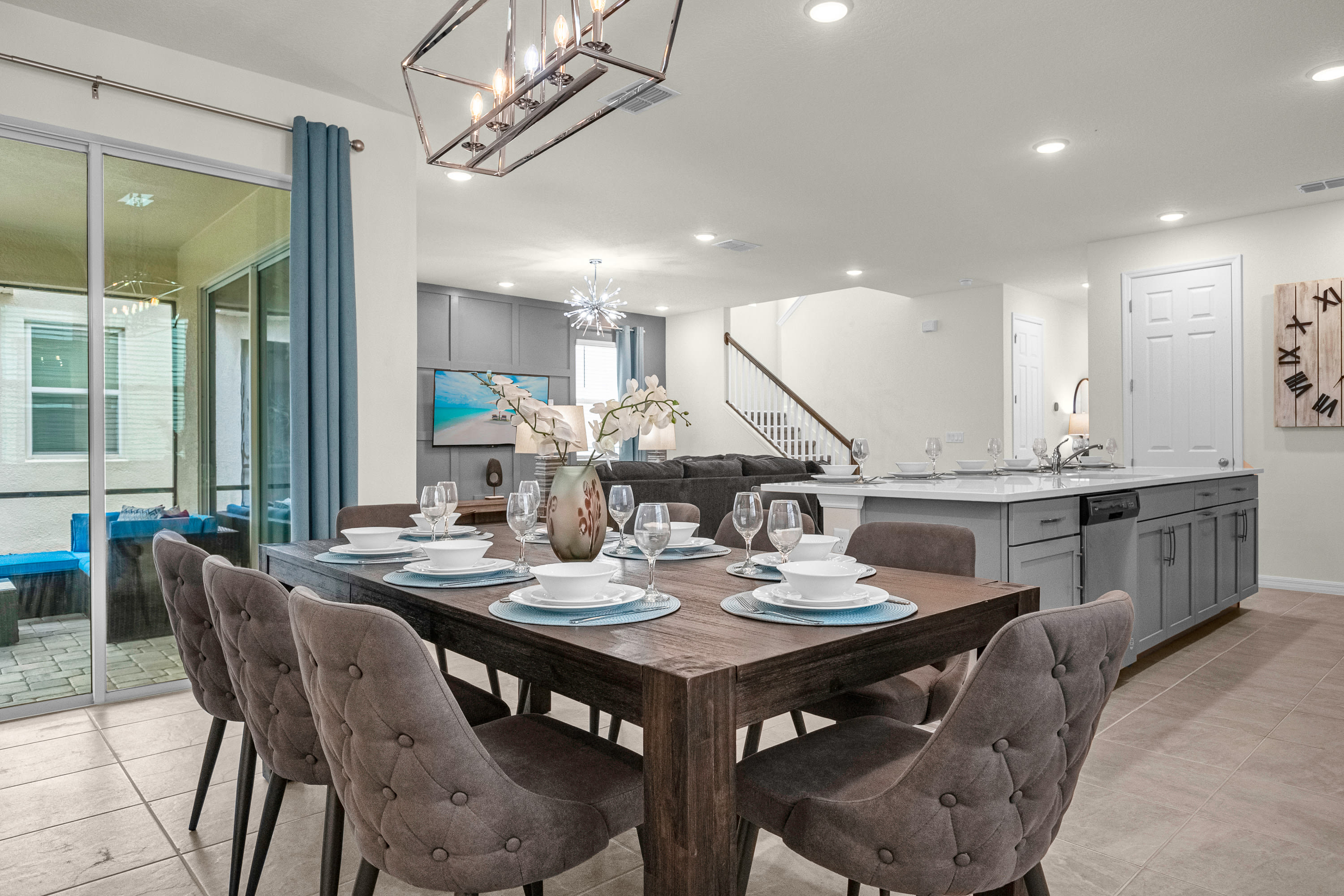 Elegant dining area with a large dark wood table set for eight, upholstered chairs, and a modern rectangular chandelier, open to the living room and kitchen.