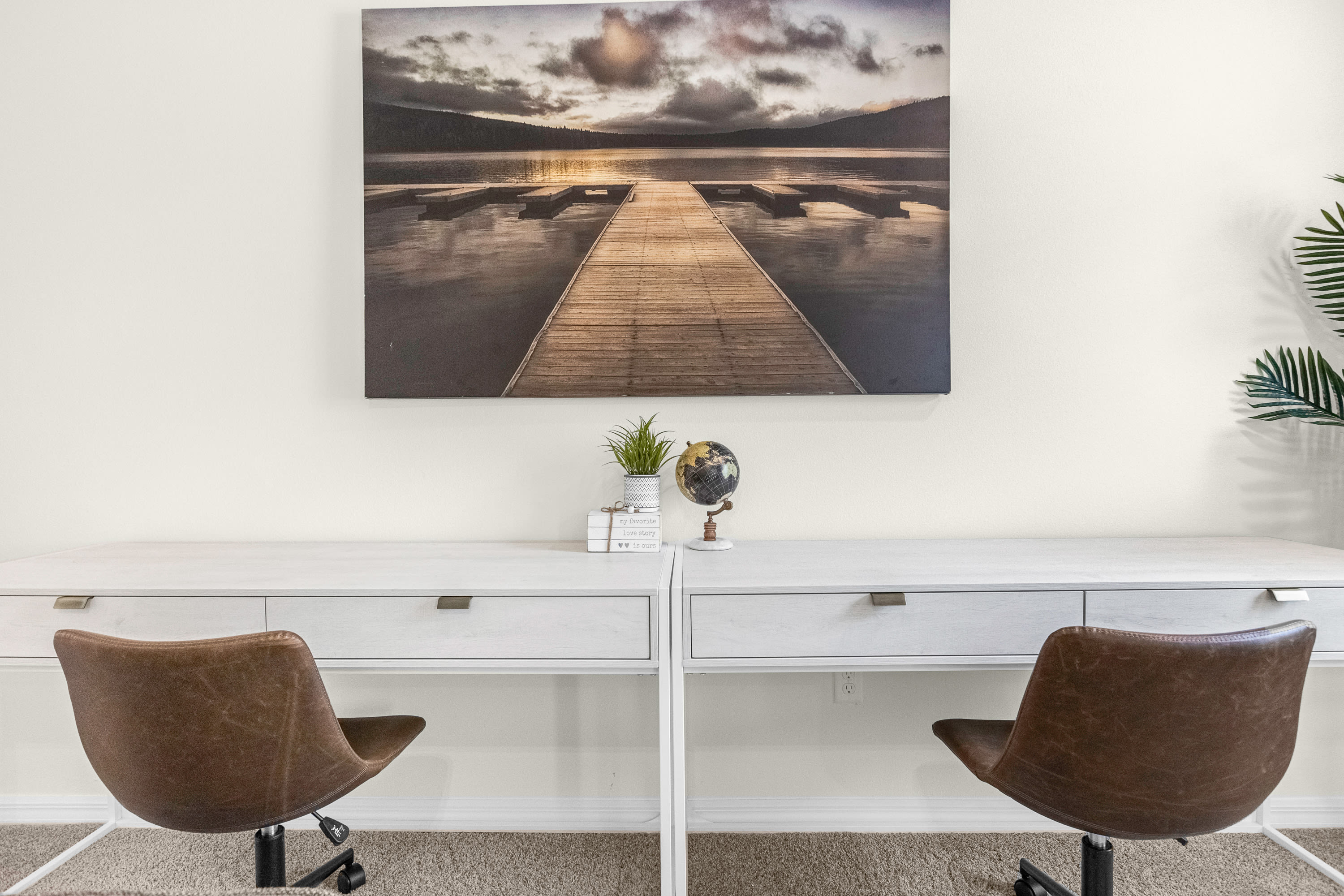 Dedicated workspace with two white desks and brown swivel chairs, set against a light-colored wall adorned with a large landscape artwork, ideal for remote work or study.
