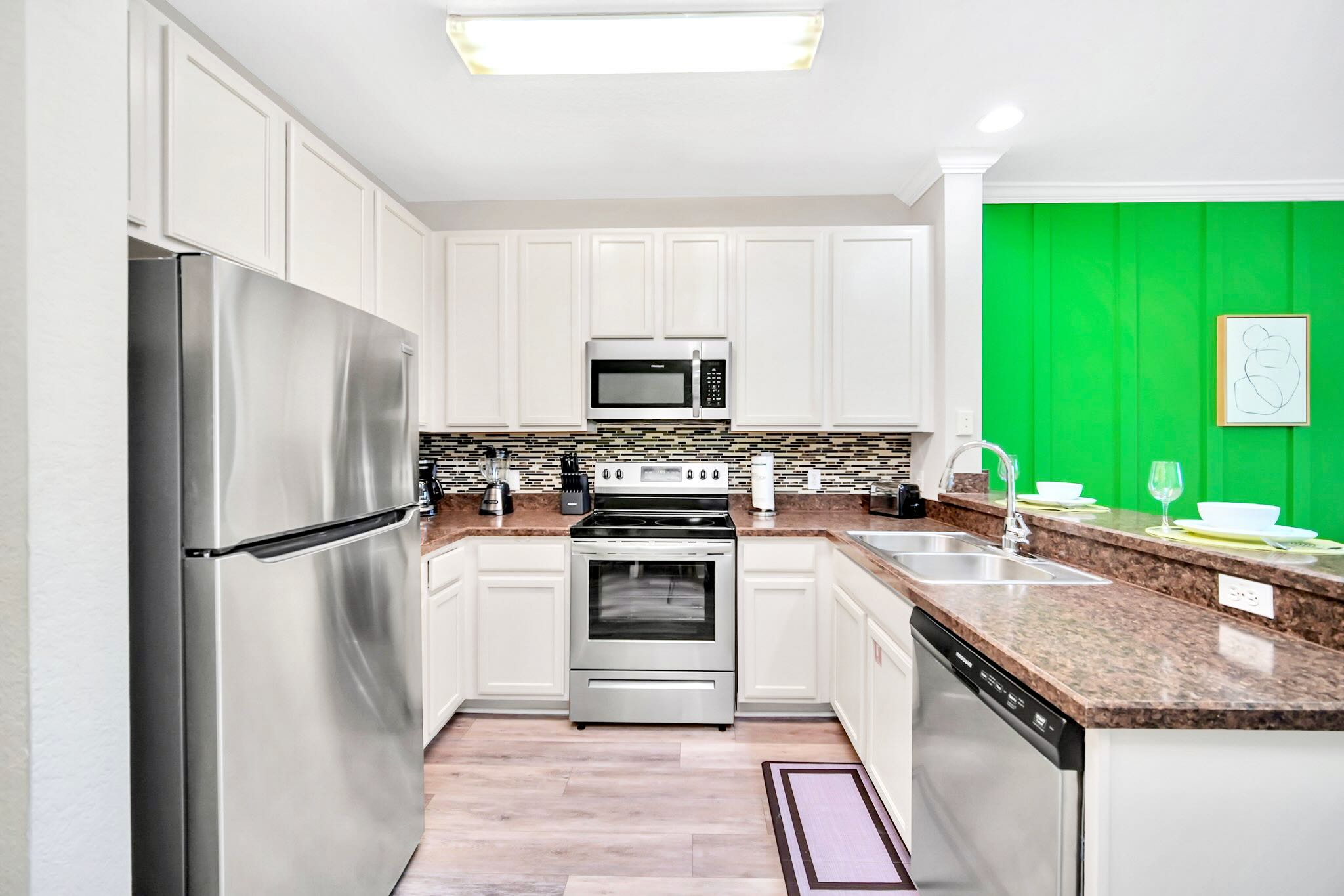 Modern kitchen with white shaker cabinets, stainless steel appliances, dark granite countertops, and a mosaic tile backsplash, featuring a vibrant green accent wall in the adjacent dining area.