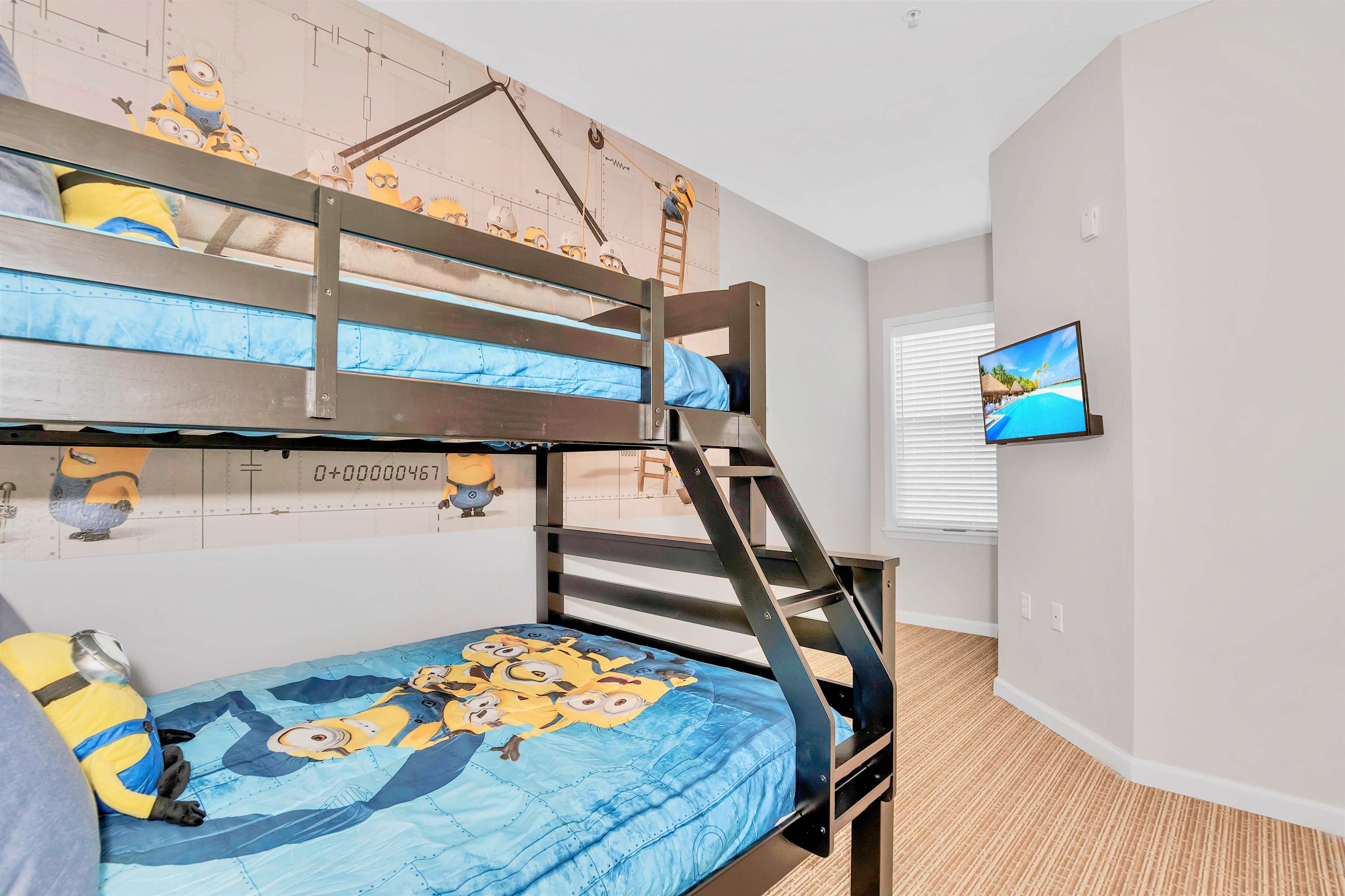 Another view of the Minions-themed kids' bedroom, showcasing the dark wooden bunk bed, a wall-mounted TV, and a window with white blinds, all contributing to a bright and playful space.