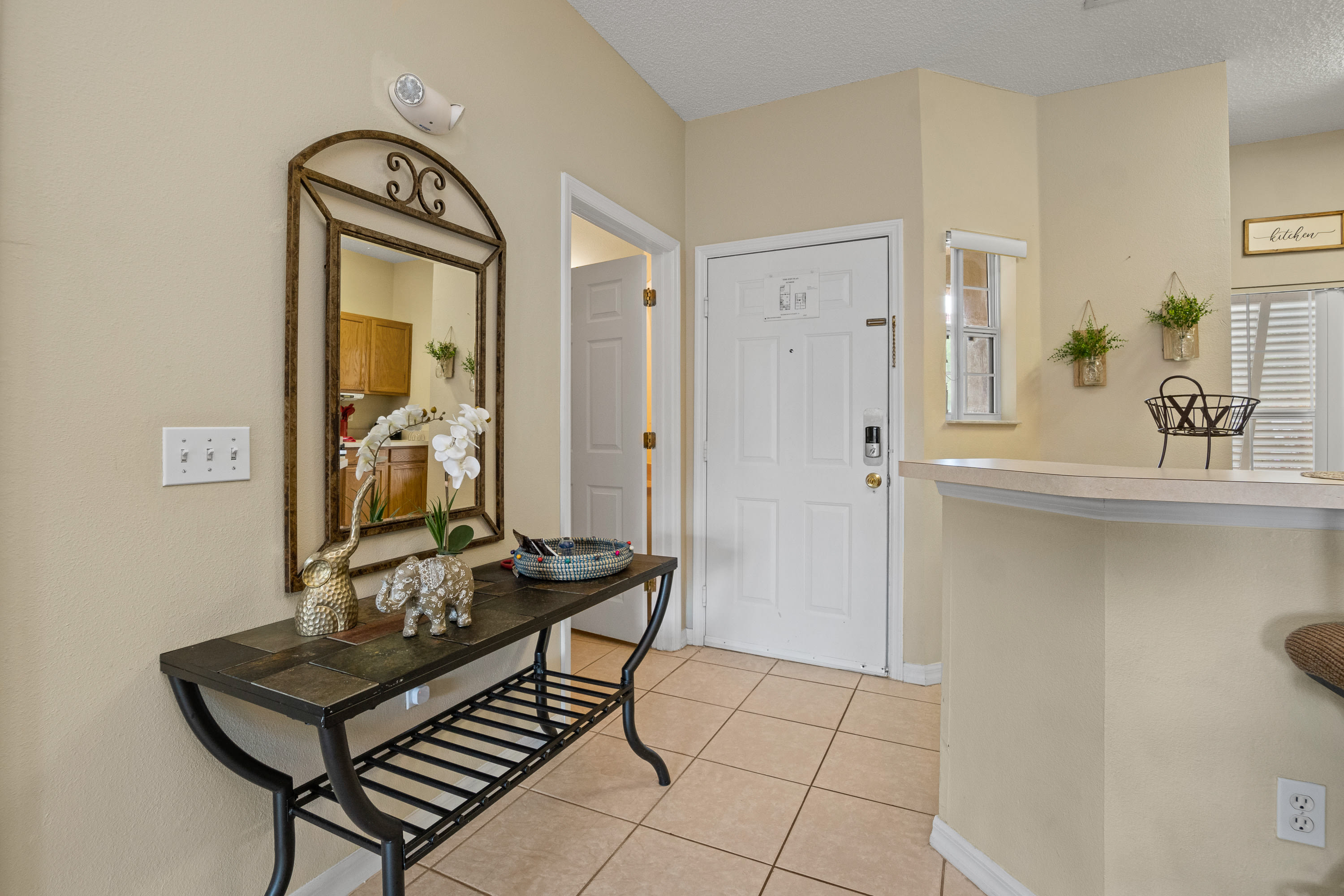 A welcoming foyer with a dark console table adorned with decorative items, a large arched mirror, and a white front door.