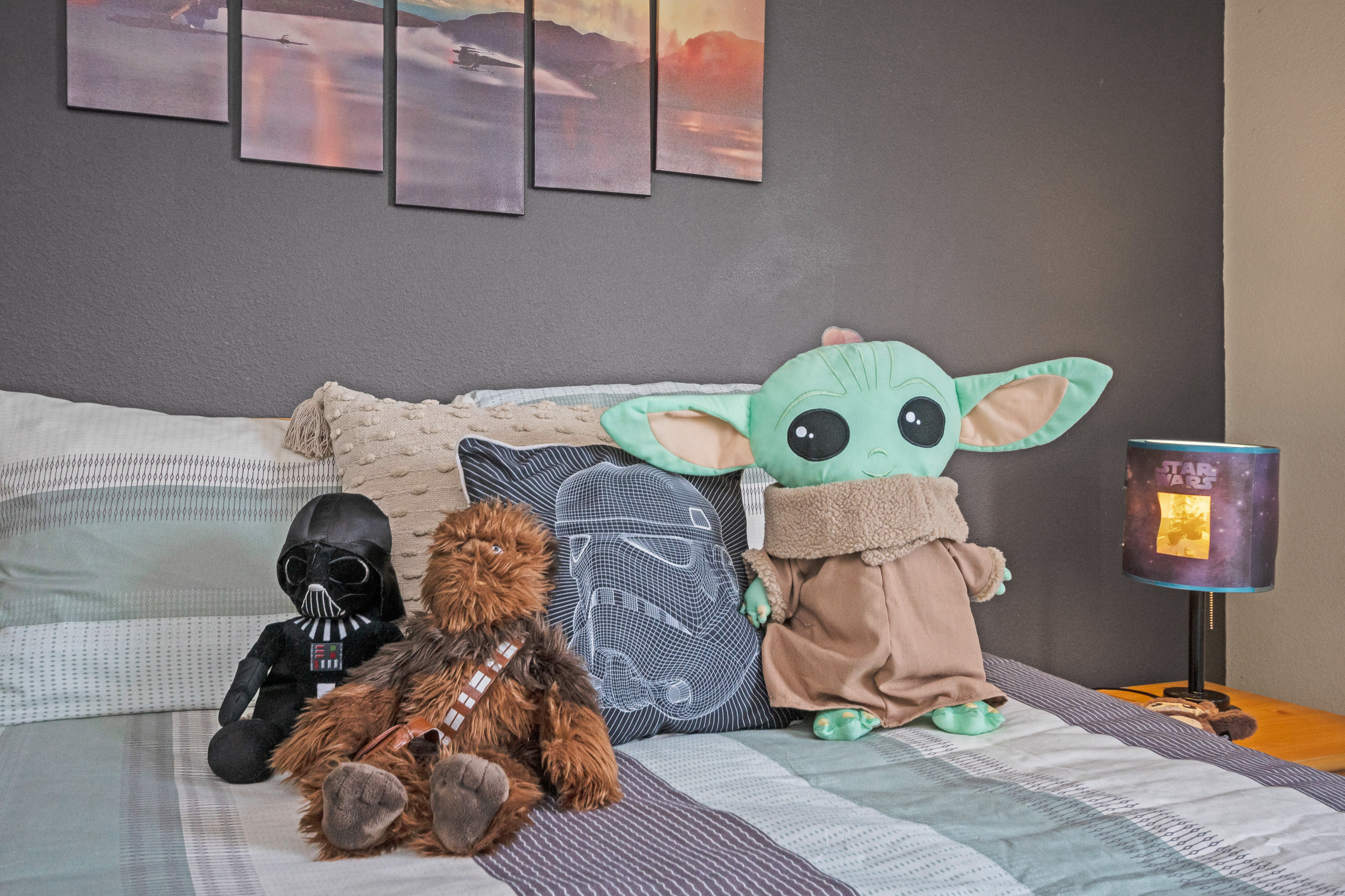 A close-up of the full-sized bed in the themed bedroom, featuring Star Wars plush toys including Grogu, Chewbacca, and Darth Vader.