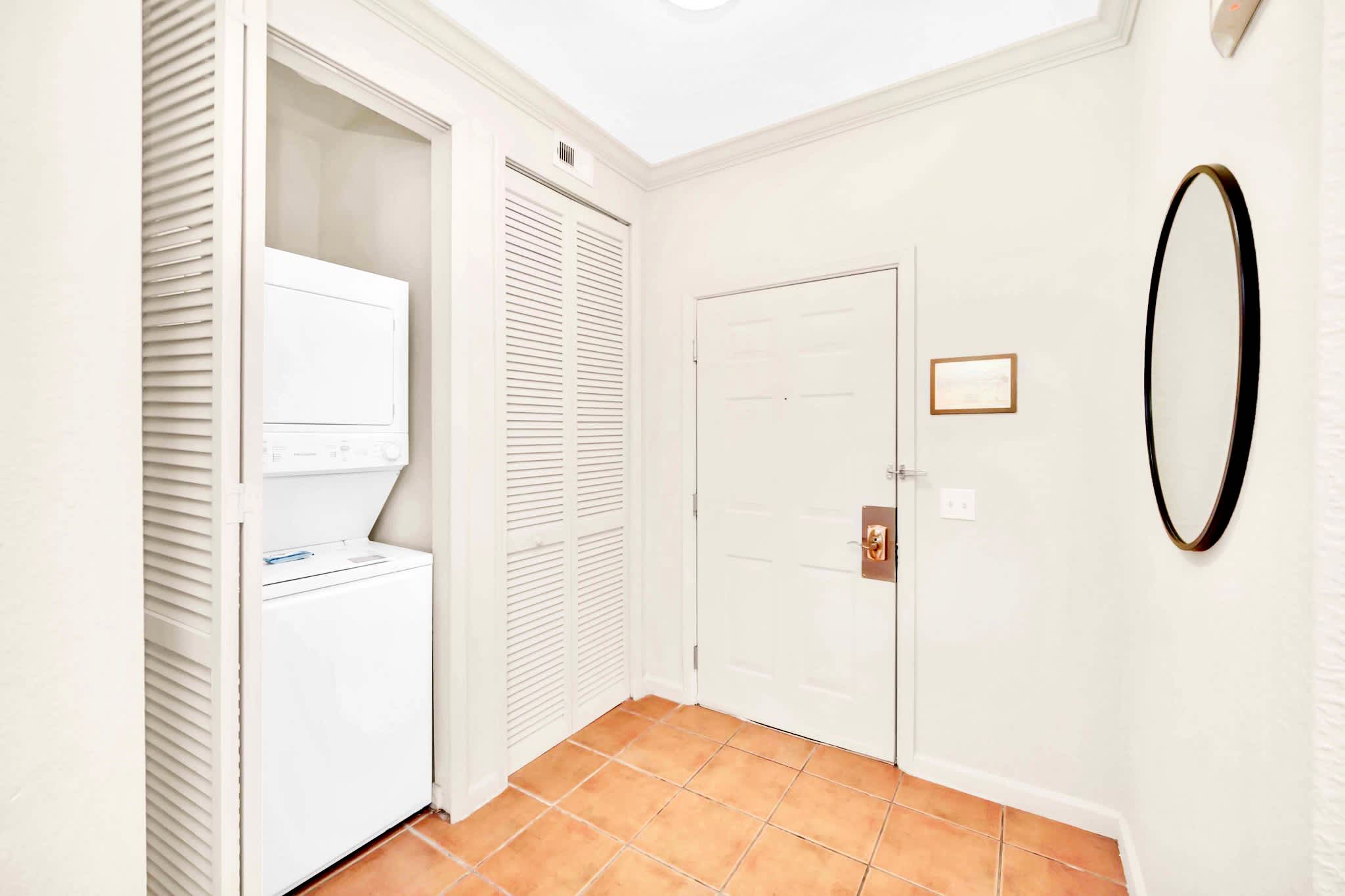 A dedicated laundry closet in the entryway featuring a white stacked washer and dryer unit behind louvered bi-fold doors. The floor is terracotta-colored tile.