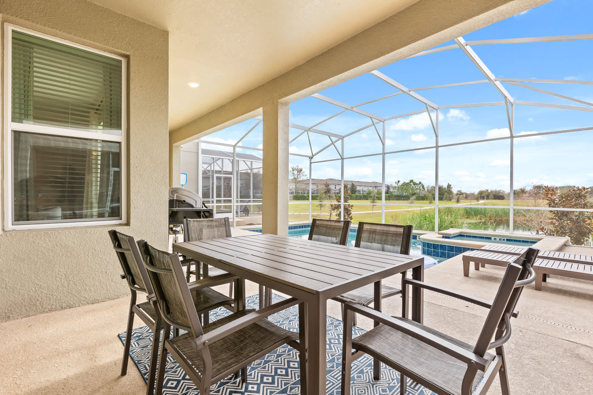 Covered outdoor patio area with a large dining table and chairs, situated next to a private screened-in pool and hot tub. The space offers views of a lake and natural surroundings, perfect for al fresco dining.