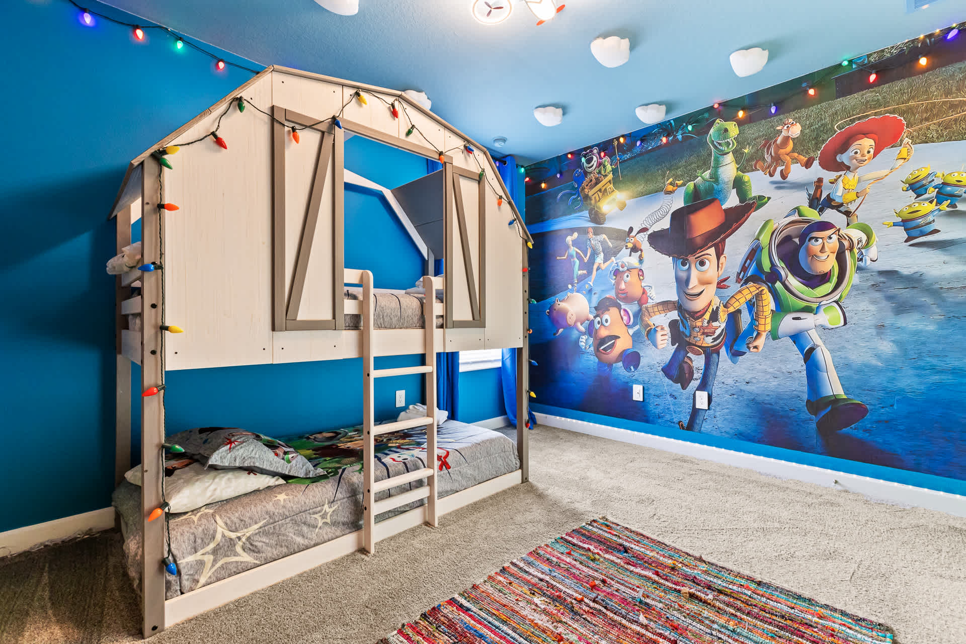 Another angle of the themed kids' bedroom, highlighting the custom barn-style bunk bed and the extensive Toy Story mural covering the blue walls, with string lights adding a festive touch.