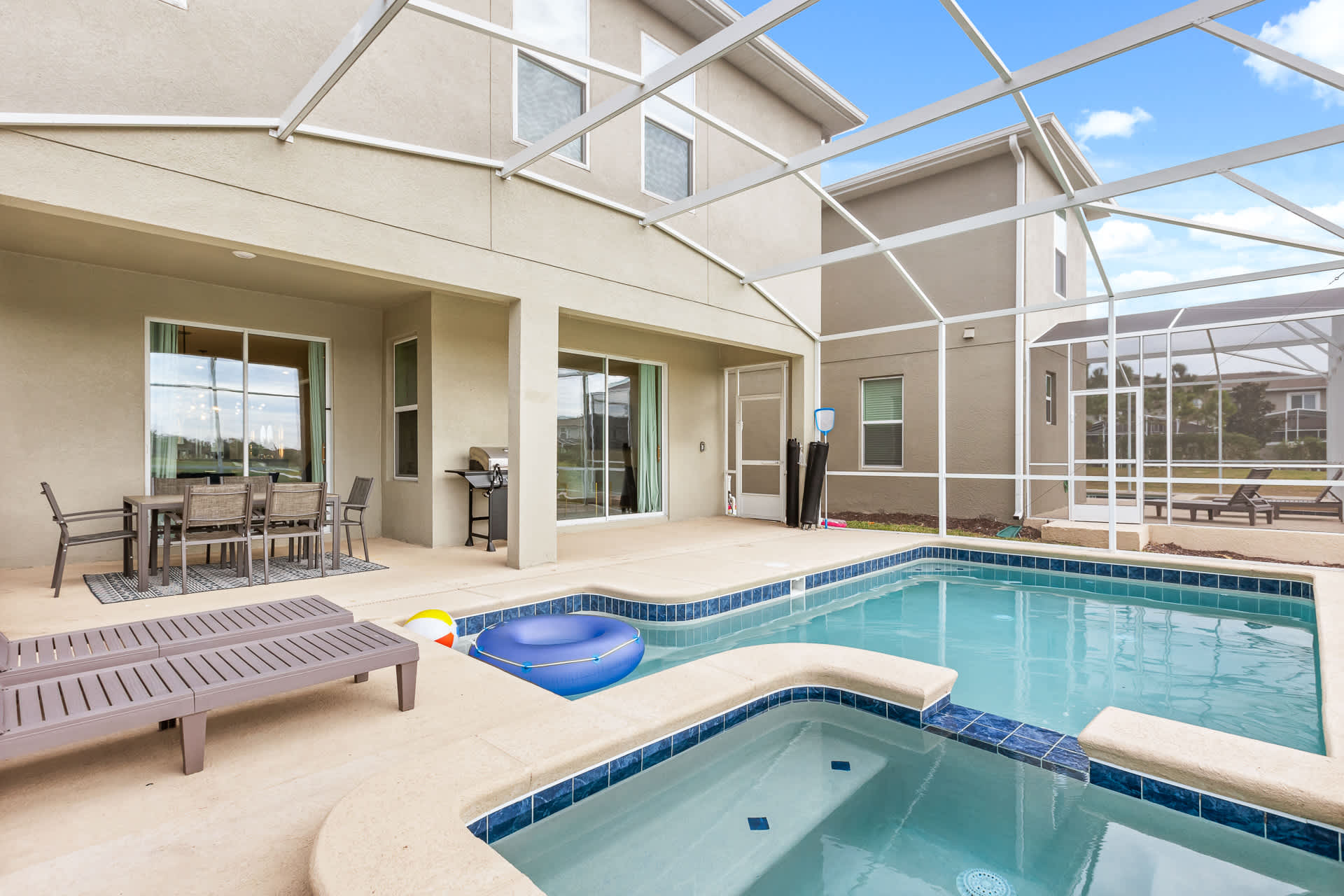 Rear exterior of the house featuring a private screened-in pool and hot tub area with a concrete deck. The modern stucco house has large windows and a covered patio, offering a private outdoor retreat.