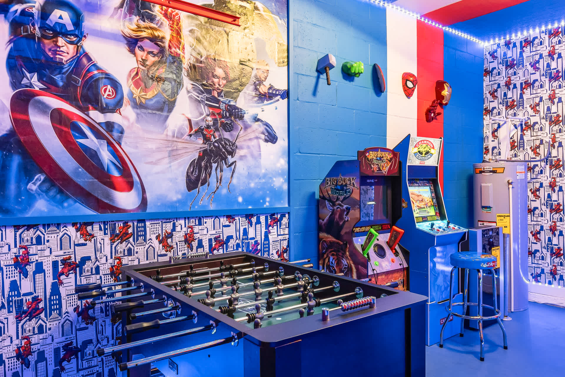 A close-up view of the Marvel-themed game room, showcasing a large Captain America mural, a foosball table, and two arcade machines, with blue LED lights accentuating the vibrant decor.