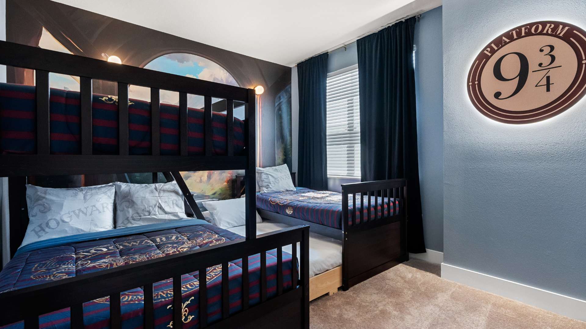 Themed children's bedroom featuring a dark wood bunk bed with blue and red striped bedding, and a matching single bed with a trundle. A large mural depicting a magical archway covers one wall, complementing the Harry Potter theme.