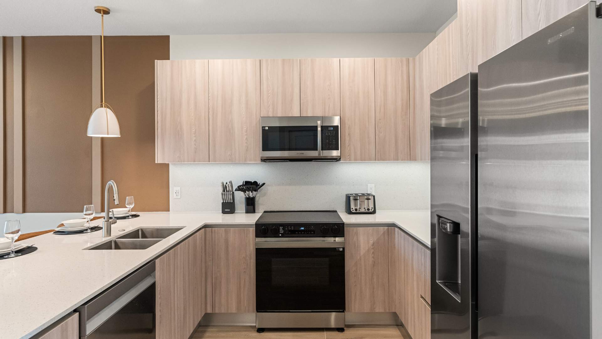 U-shaped kitchen with light wood cabinets, white quartz countertops, and stainless steel appliances including a microwave, electric range, and refrigerator. A toaster and coffee maker are visible on the counter.