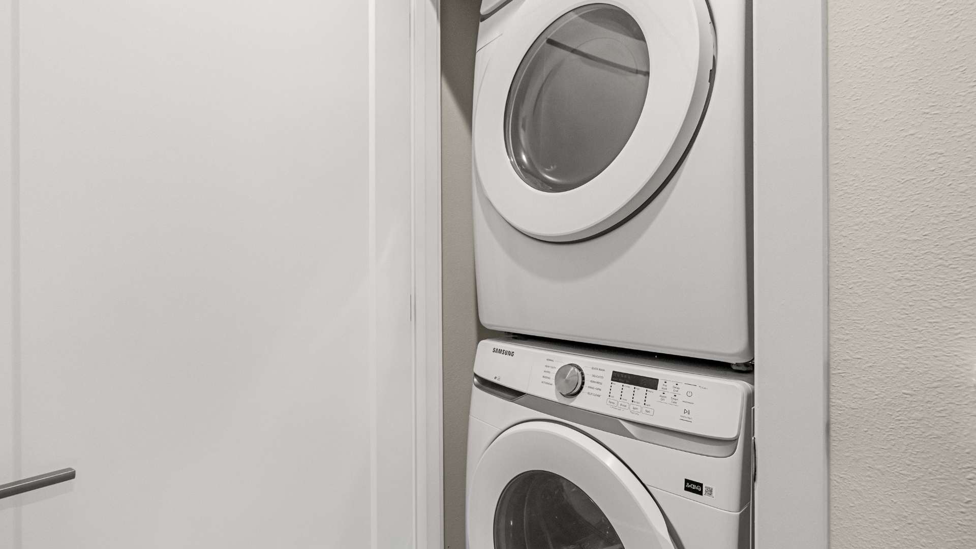 Compact laundry area featuring a stacked white Samsung washer and dryer unit, neatly tucked into a closet space. The appliances are modern and clean, ready for guest use.