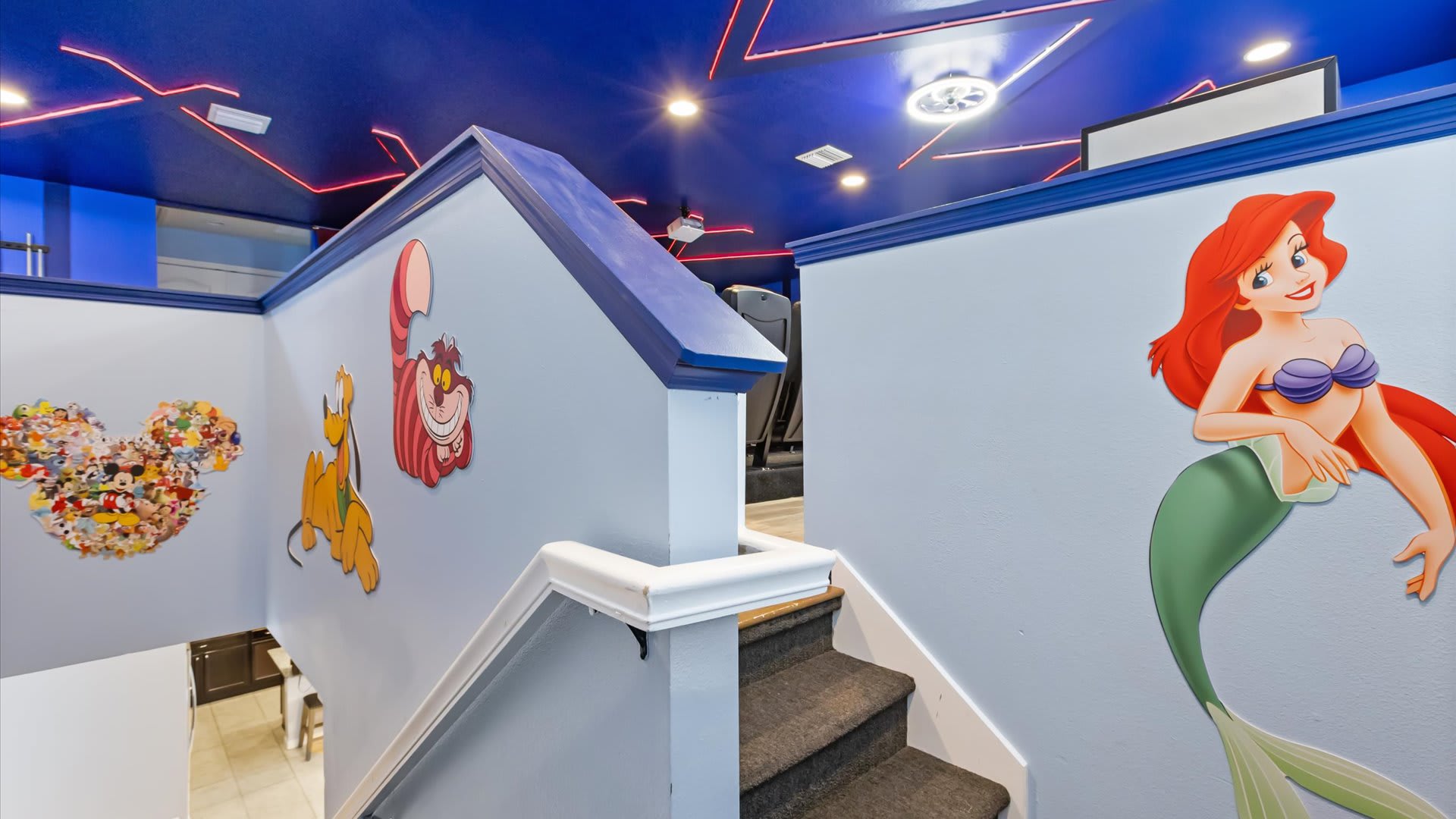 A vibrant staircase area features light blue walls adorned with large Disney character cutouts, including Ariel, Pluto, and the Cheshire Cat. The stairs are carpeted, and a blue railing leads up to another level.