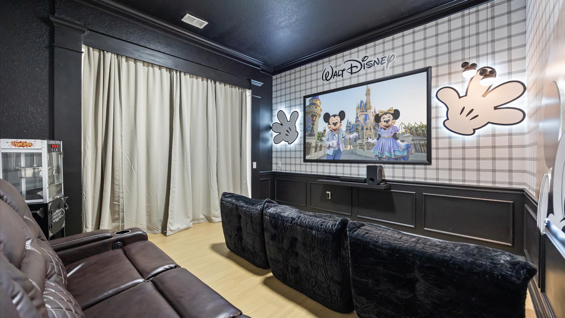 Themed media room with a large projection screen, two rows of seating including plush beanbag-style chairs and a leather recliner sofa, and a vintage popcorn machine.