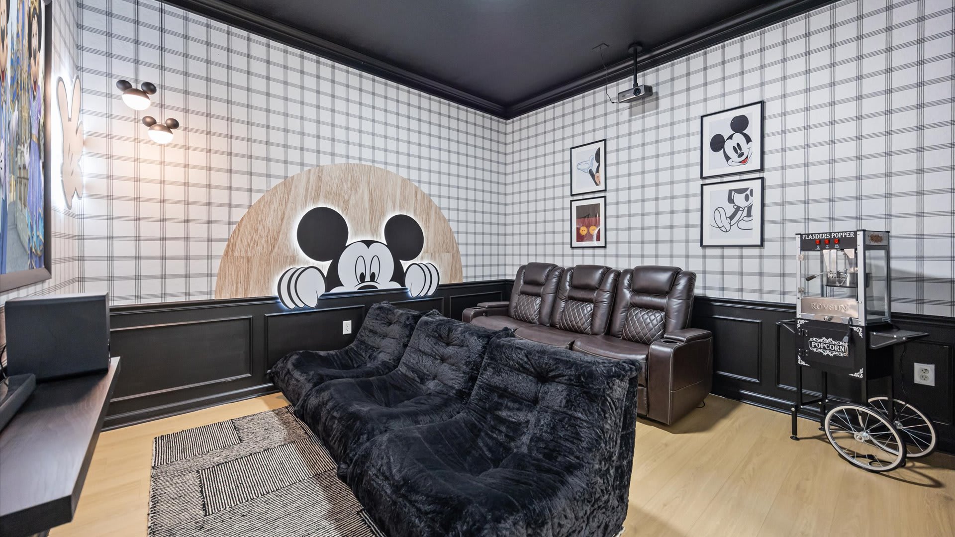 Playful media room featuring plaid wallpaper, black wainscoting, Mickey Mouse wall art, a leather recliner sofa, and plush beanbag seating, with a popcorn machine in the corner.