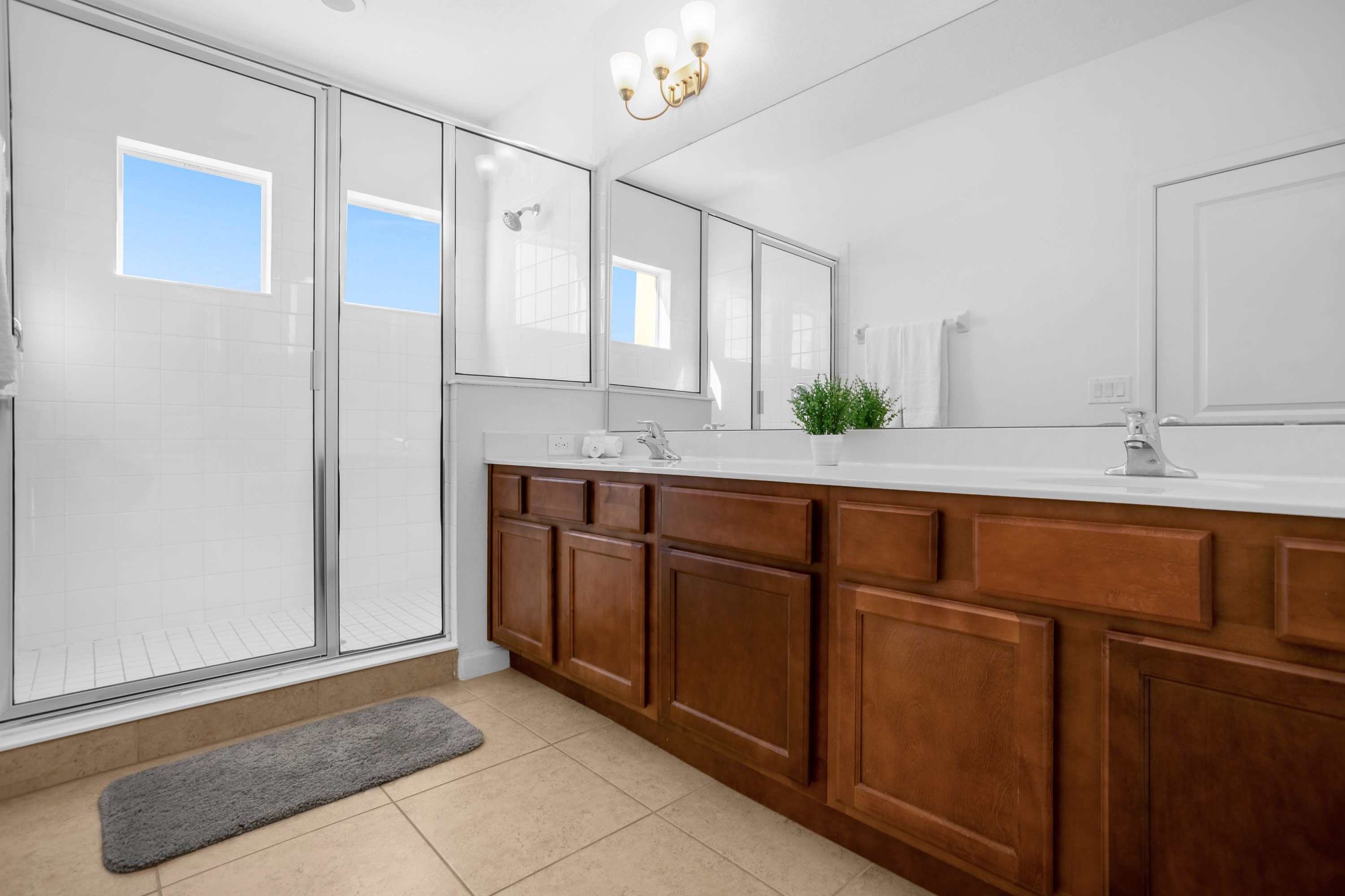 Modern bathroom featuring a glass-enclosed shower with white subway tiles, a long double vanity with dark wood cabinets and white countertops, and a large mirror reflecting the room.