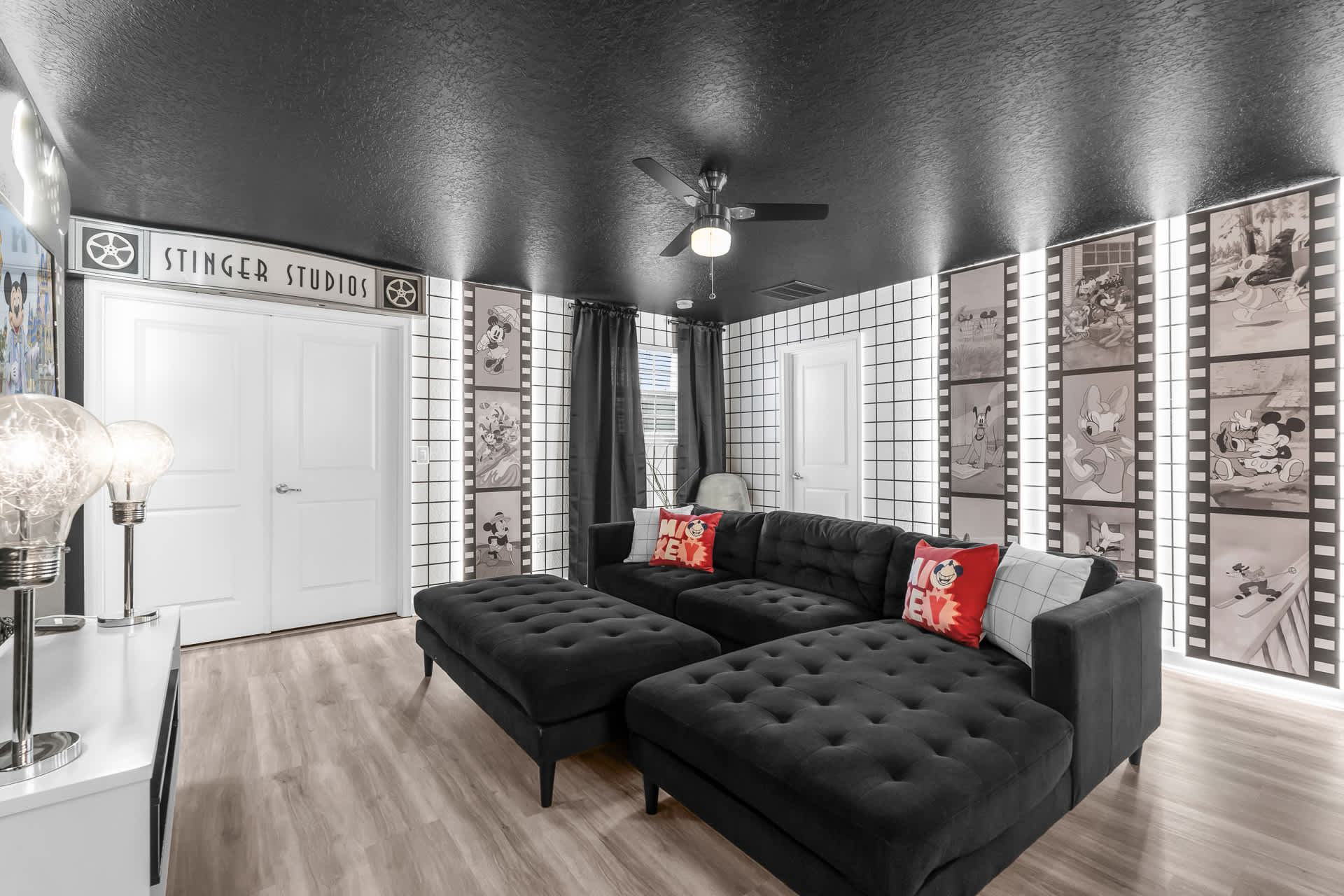 Themed media room with a black sectional sofa, black ceiling, and walls adorned with large film strip graphics featuring classic cartoon characters, creating an immersive entertainment space.