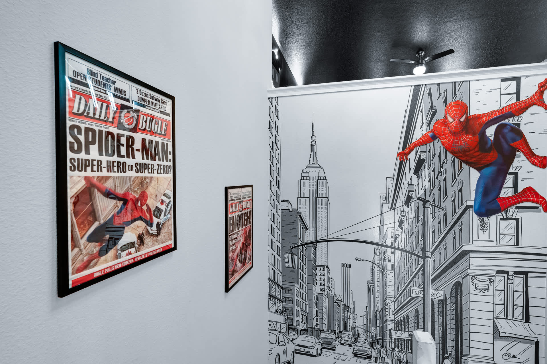 Themed hallway featuring a vibrant Spiderman mural on a black and white cityscape background, with framed 'Daily Bugle' posters on the adjacent light grey wall, leading to a dark ceiling area.