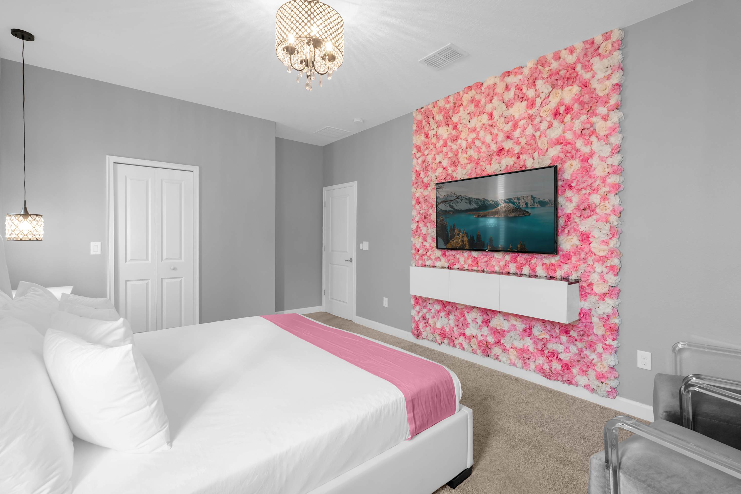 Stylish bedroom with a large TV mounted on a vibrant pink floral wall, a white upholstered bed, and light grey walls, offering a luxurious and visually striking sleeping space.