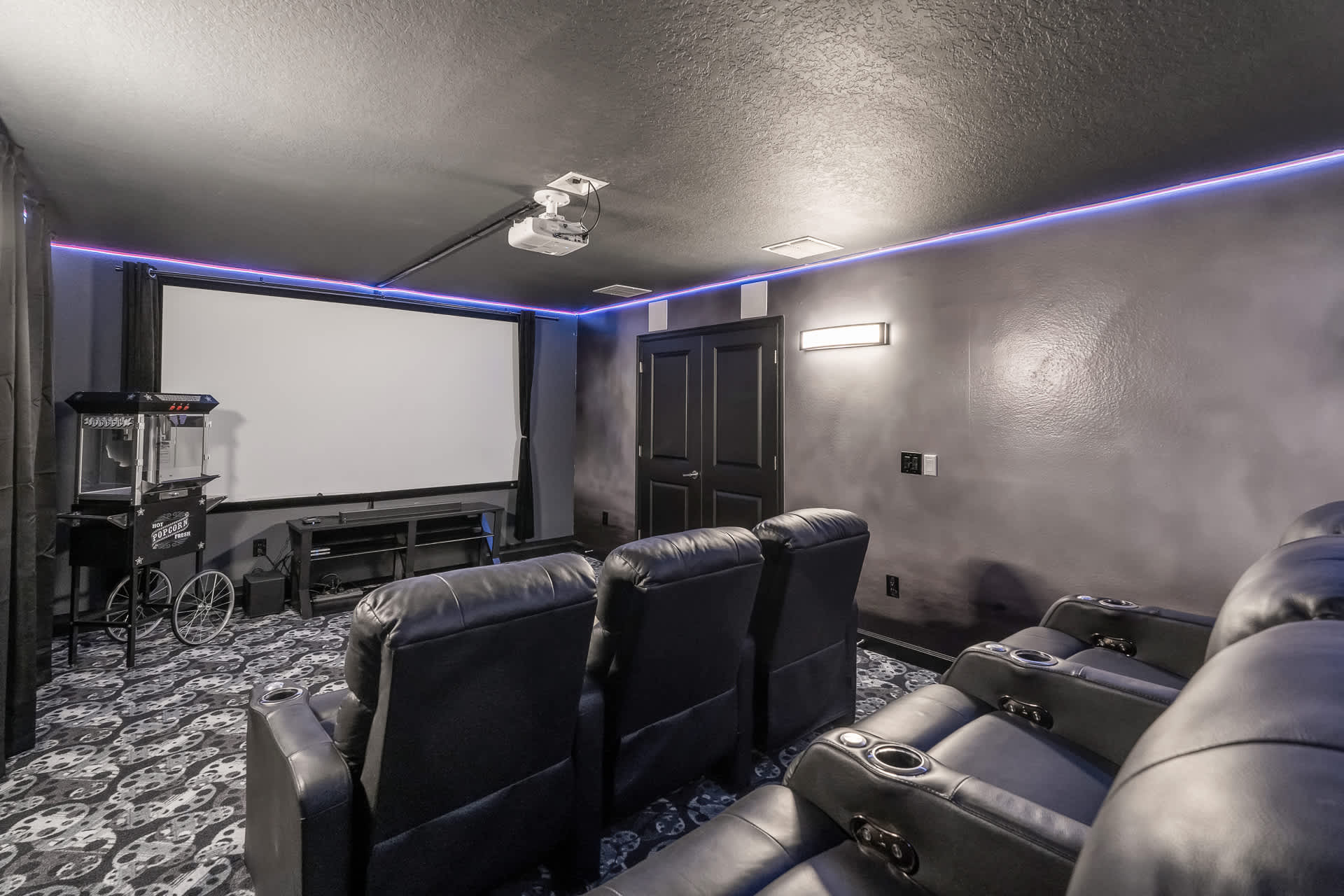 A dedicated media room features a large projection screen, a popcorn machine, and multiple rows of comfortable black reclining theater seats on a patterned carpet.