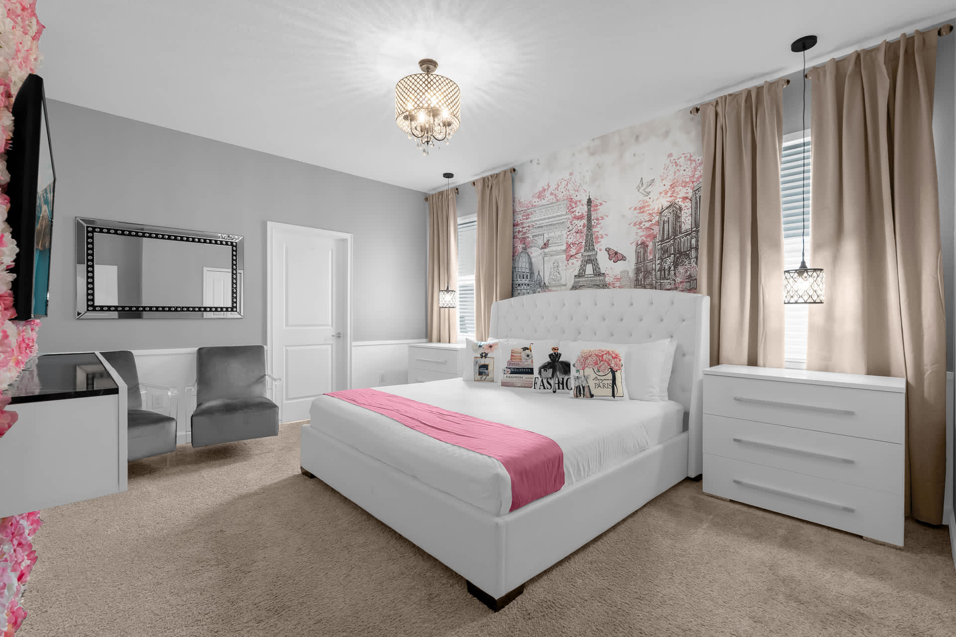 Elegant bedroom featuring a white upholstered bed with a pink throw, a feature wall with a floral and Eiffel Tower mural, light grey walls, and a gold chandelier, creating a chic Parisian theme.