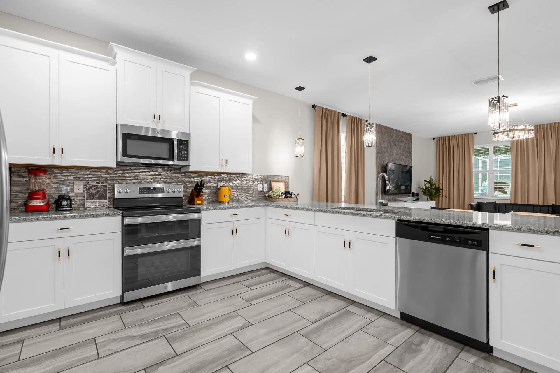 Contemporary kitchen with white shaker cabinets, stainless steel double oven range, microwave, and dishwasher, complemented by a grey mosaic tile backsplash and light grey tiled flooring.