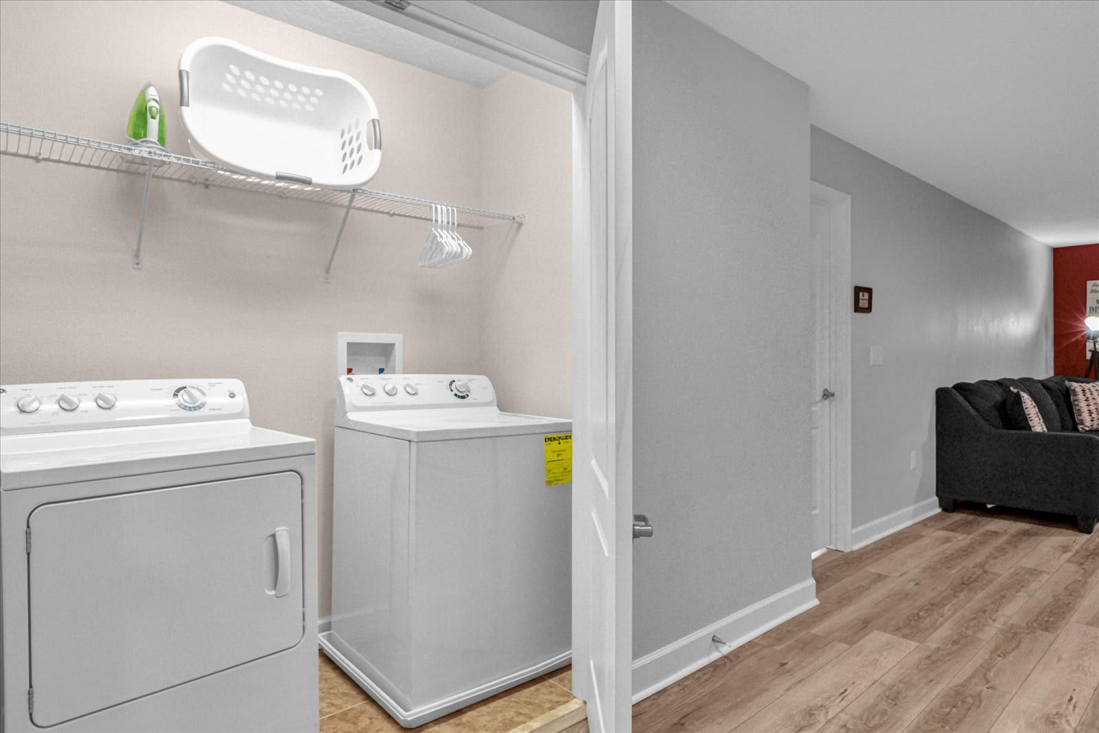 Dedicated laundry area with a white top-loading washing machine and a white dryer, a wire shelf with a laundry basket and hangers, and light beige walls.