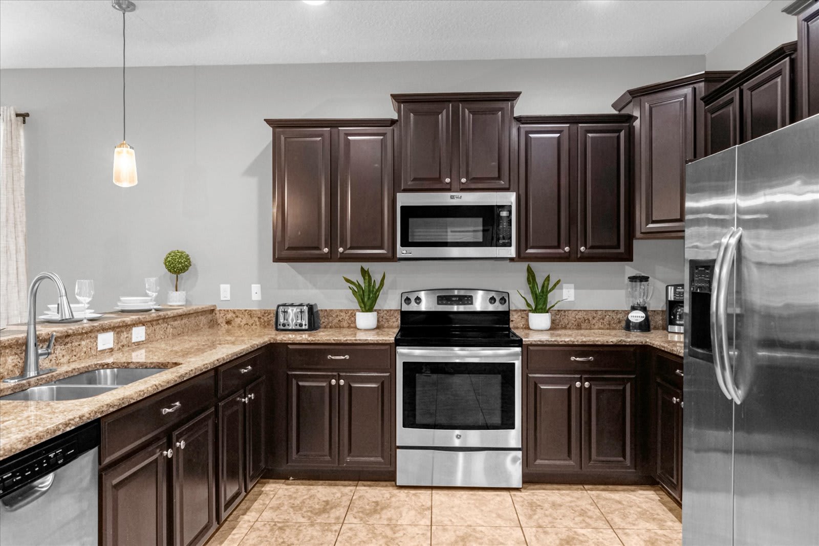Full view of the kitchen featuring dark wood cabinetry, granite countertops, and stainless steel appliances including a range, microwave, and dishwasher. Decorative plants add a touch of greenery to the space.