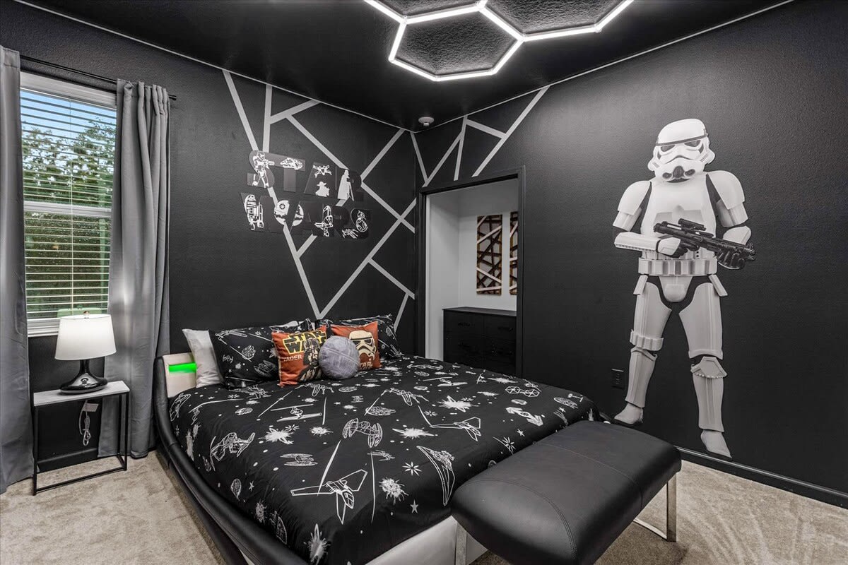 Dark and dramatic Star Wars themed bedroom with black walls, geometric white accents, a queen-sized bed with themed bedding, and a large Stormtrooper decal.