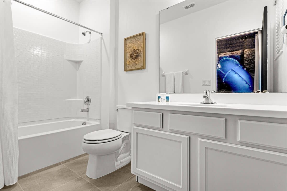 Bright white bathroom with a single vanity, a toilet, and a shower/tub combo, reflecting the blue slide from the adjacent Harry Potter themed bedroom.