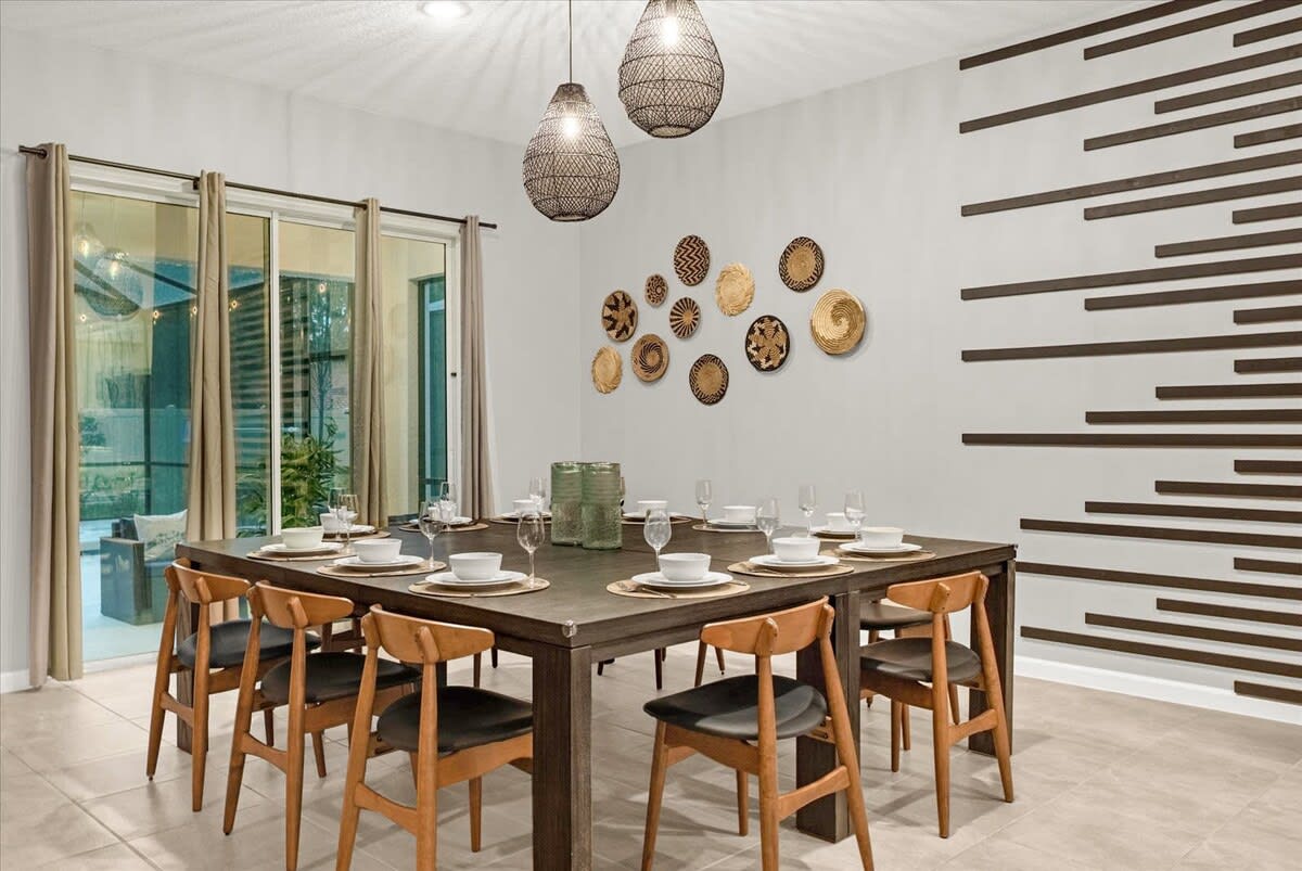 A modern dining room features a large square dark wood dining table set for eight, with light wood chairs and black seats. The wall is decorated with woven baskets and horizontal dark wood slats, illuminated by two large woven pendant lights.