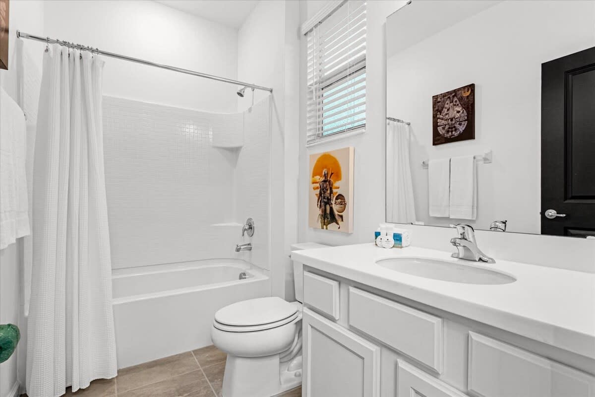 Modern white bathroom featuring a single vanity with a white countertop, a toilet, and a shower/tub combo, with Star Wars themed art on the wall.