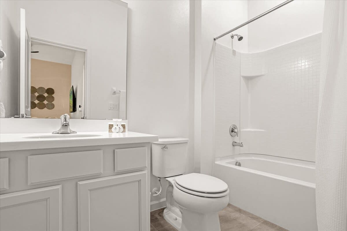 Compact white bathroom with a single vanity, a toilet, and a shower/tub combo with white subway tile surround. The floor is tiled.