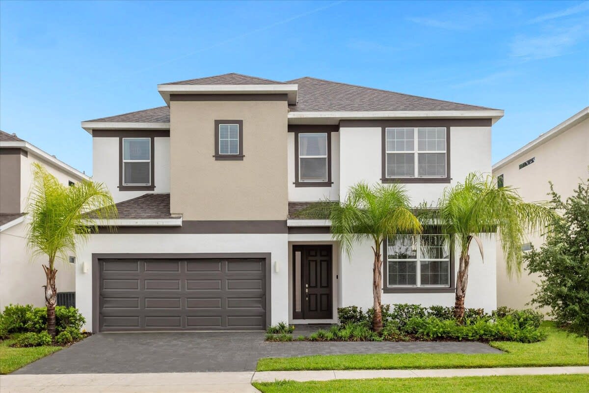 A modern two-story house with a white and beige facade, dark trim, and a dark gray garage door. Palm trees flank the entrance, and a well-maintained lawn and driveway are visible.