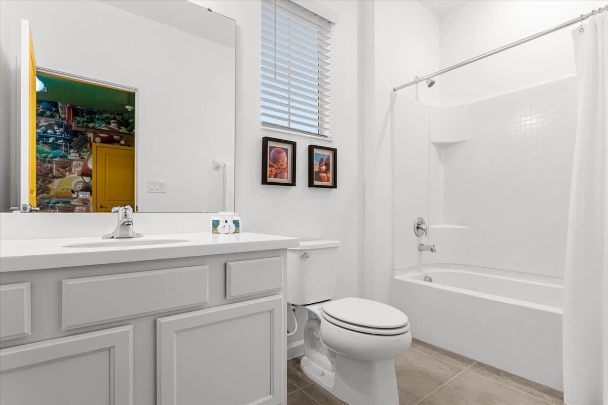 Clean white bathroom featuring a single vanity with a white countertop, a toilet, and a shower/tub combo with white subway tile, reflecting the colorful themed bedroom.