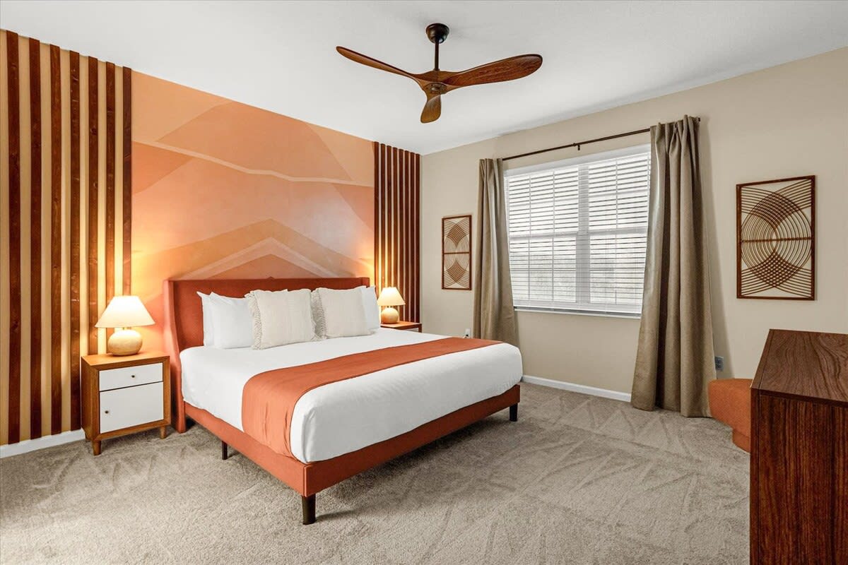Warm-toned bedroom with a large bed, an orange bed frame, and a striking accent wall with vertical wooden slats and geometric patterns. Two nightstands with lamps flank the bed.