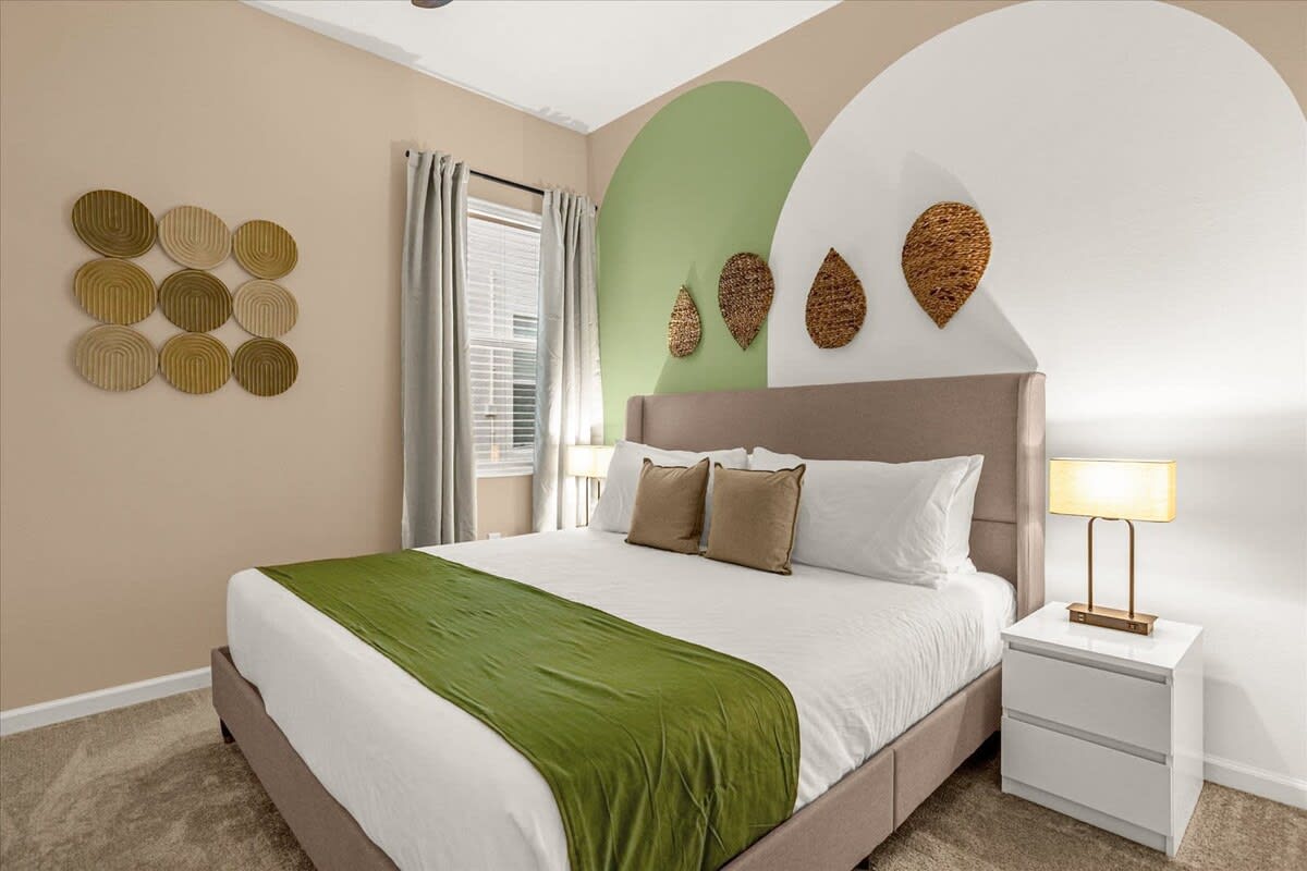 Cozy bedroom with a large bed, a green bed runner, and a unique accent wall featuring green and white arched shapes. Woven wall art decorates the wall.
