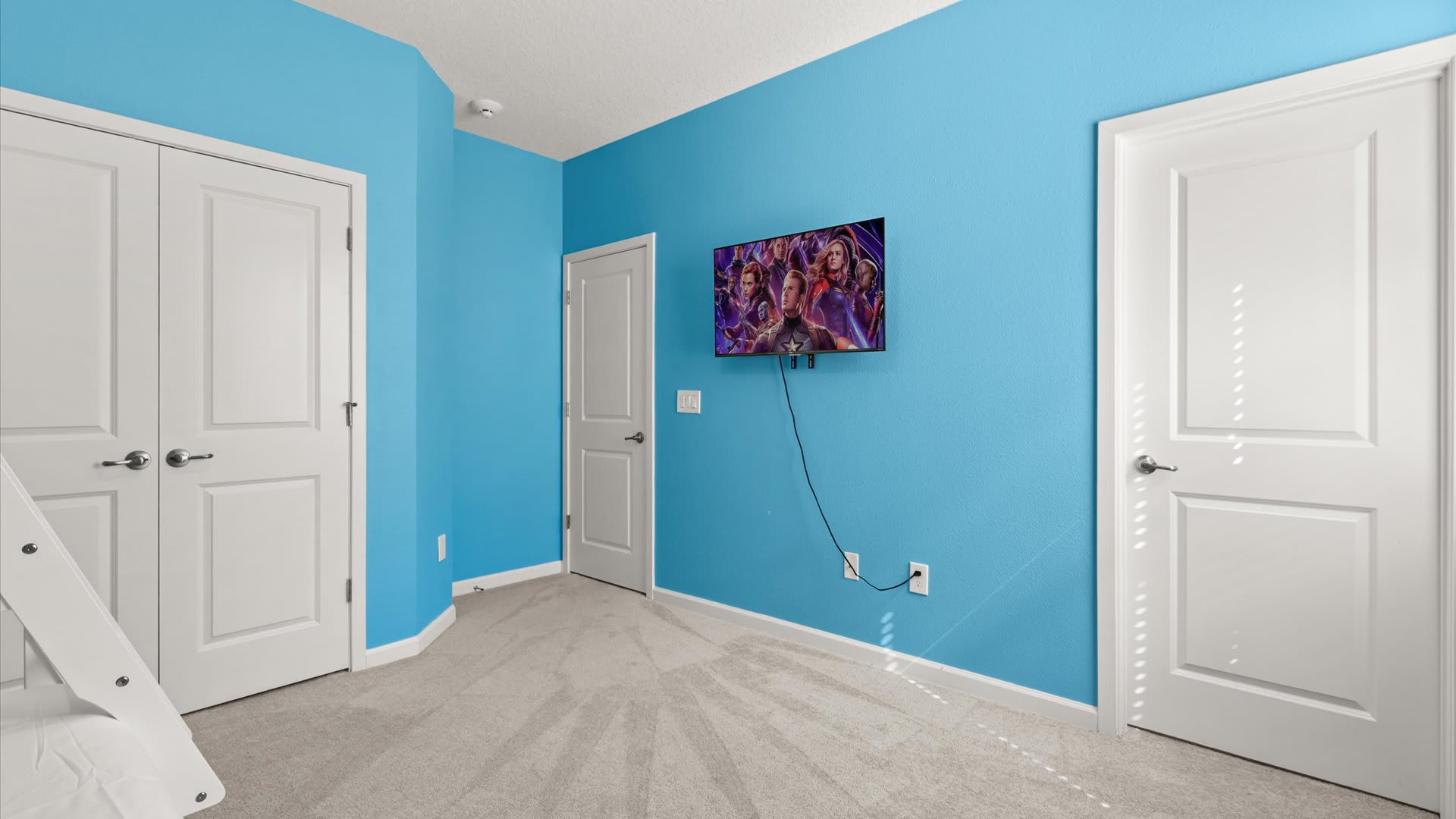 View of a themed kids' bedroom with bright blue walls, showing a wall-mounted TV displaying a movie scene. White doors are visible, including bi-fold closet doors.