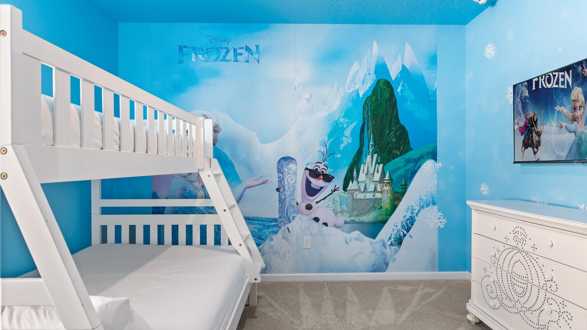 Another view of the "Frozen" themed kids' bedroom, showcasing the white wooden bunk bed, the expansive blue mural with Elsa and Olaf, and a white dresser with intricate carvings.