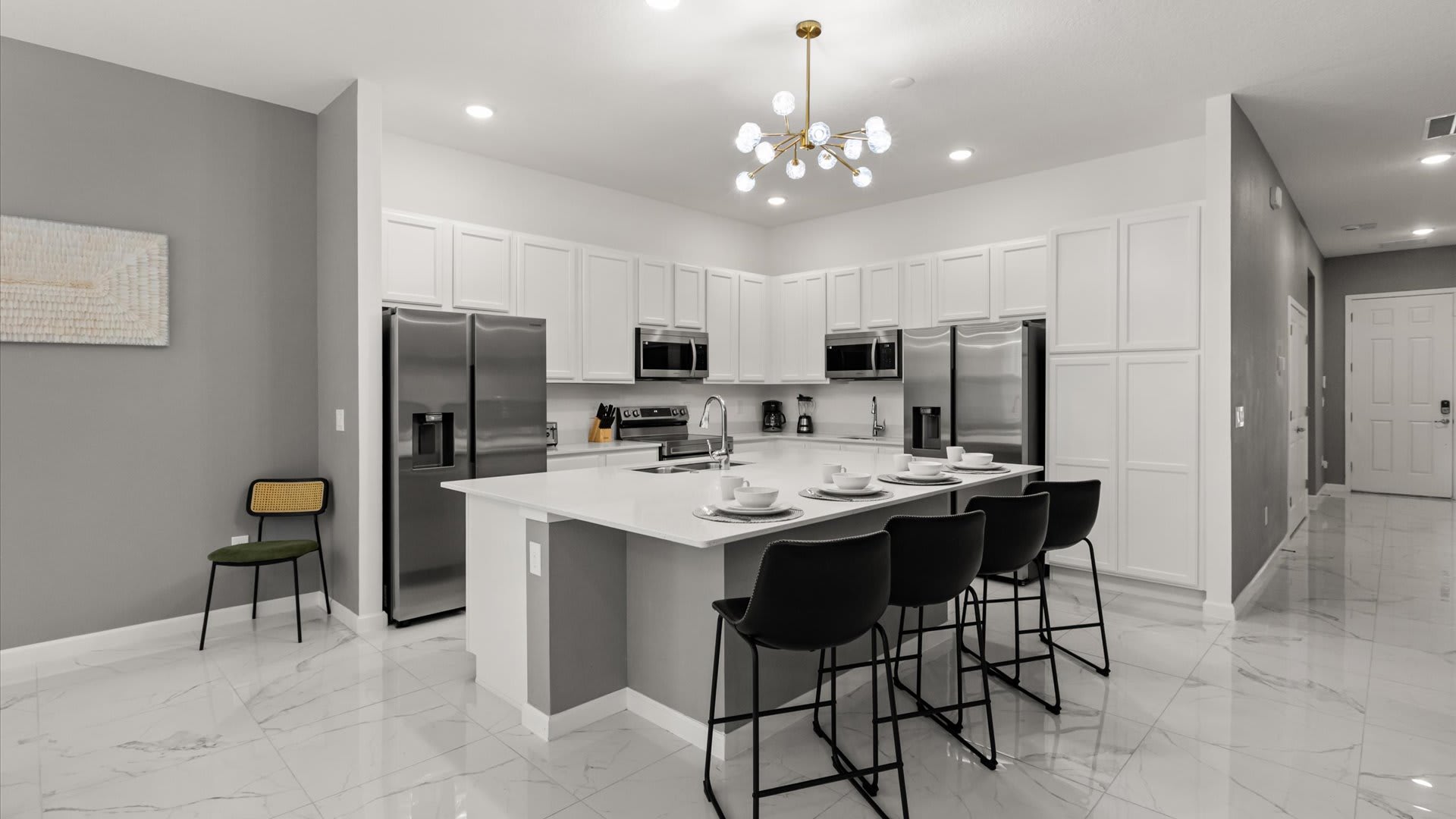 Bright, modern kitchen with white shaker cabinets, stainless steel appliances, and a large island with a white countertop and seating for four on black bar stools. A contemporary sputnik chandelier illuminates the space.