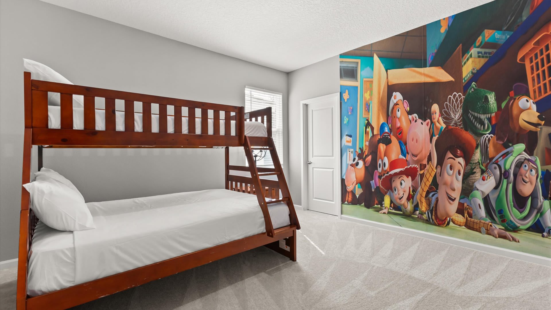 A vibrant kids' bedroom features a wooden bunk bed with white bedding against a colorful Toy Story mural wall. The room has light gray walls and a window with blinds.