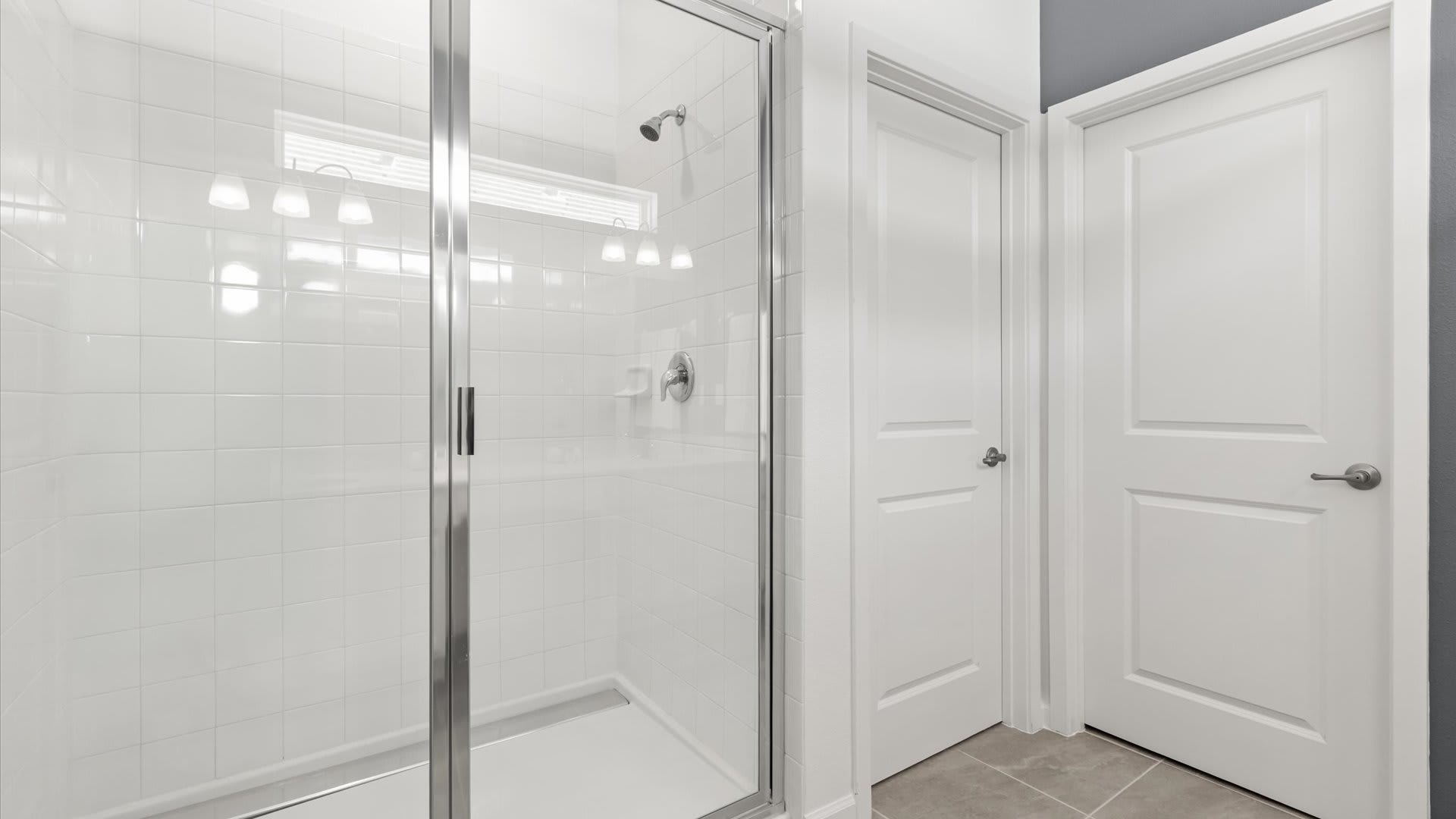 Bright, modern shower stall with white subway tiles, a glass enclosure, and a chrome shower head. A small window above provides natural light.