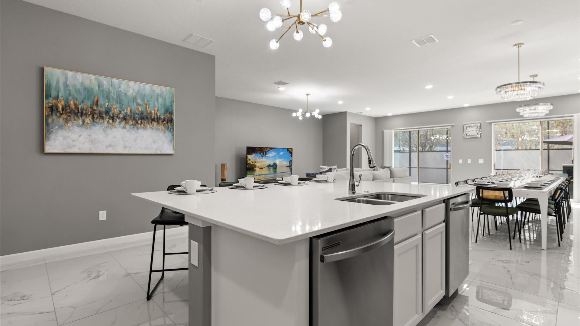 Close-up view of the kitchen island with a sink and dishwasher, showing white quartz countertops and black bar stools. The open-concept layout reveals the dining area and living room in the background.