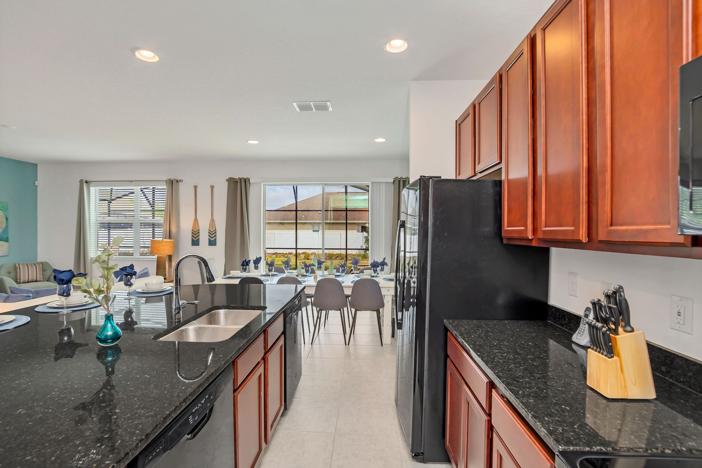 Modern kitchen featuring dark cherry wood cabinets, sleek black granite countertops, and black appliances, including a double sink. A central island with bar seating overlooks the adjacent dining and living areas, promoting an open-concept design.