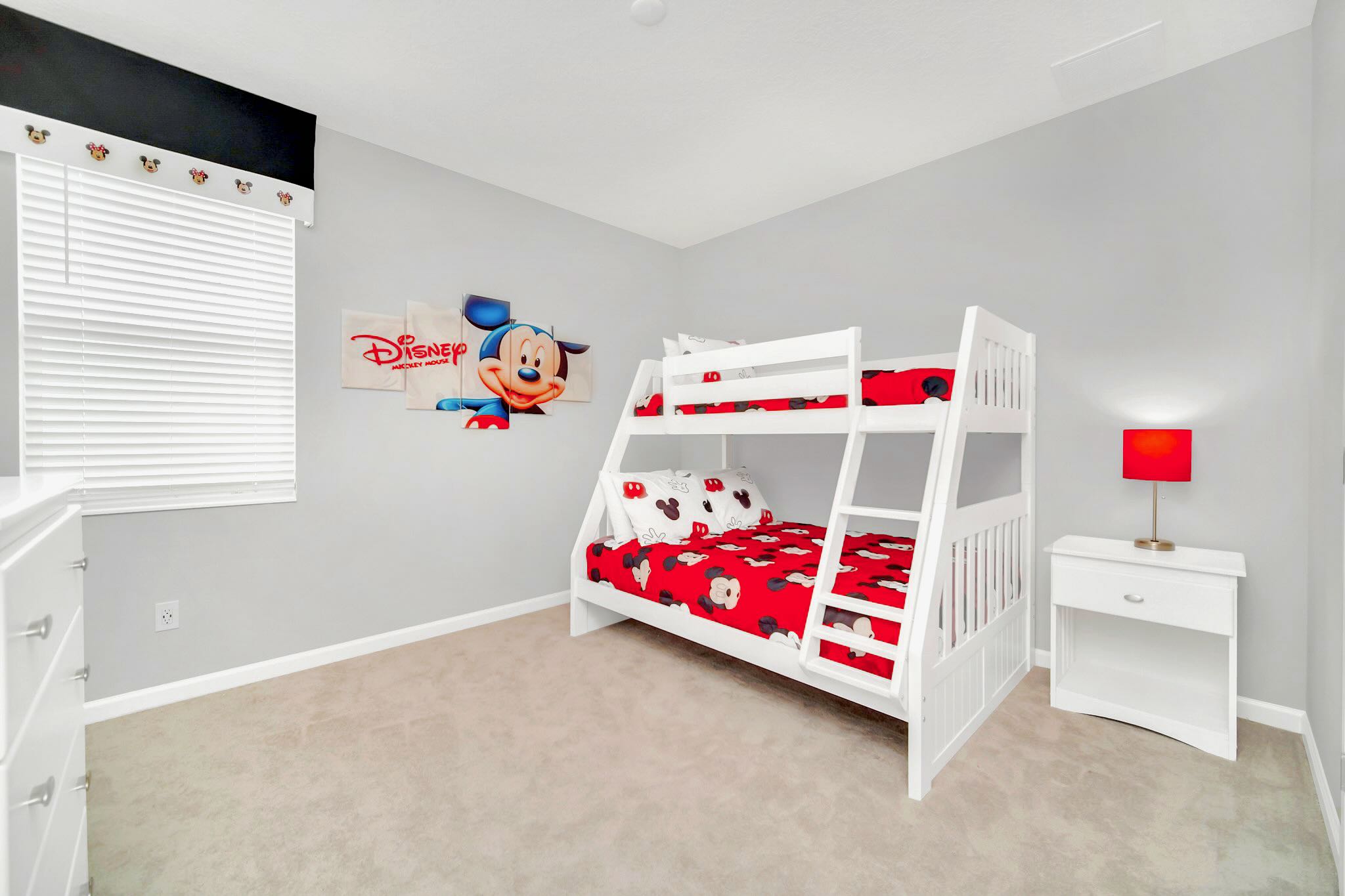 Kids' bedroom with light gray walls, a white bunk bed featuring red and white Mickey Mouse bedding, and a matching white nightstand with a red lamp. Large Mickey Mouse wall art is displayed above the bed.