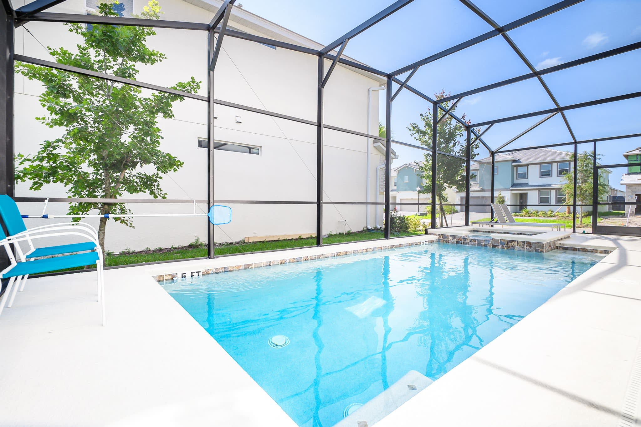 A clear blue private swimming pool with a shallow end marked "5 FT" is visible within a screened enclosure, featuring a small hot tub section and a blue and white chair on the patio.